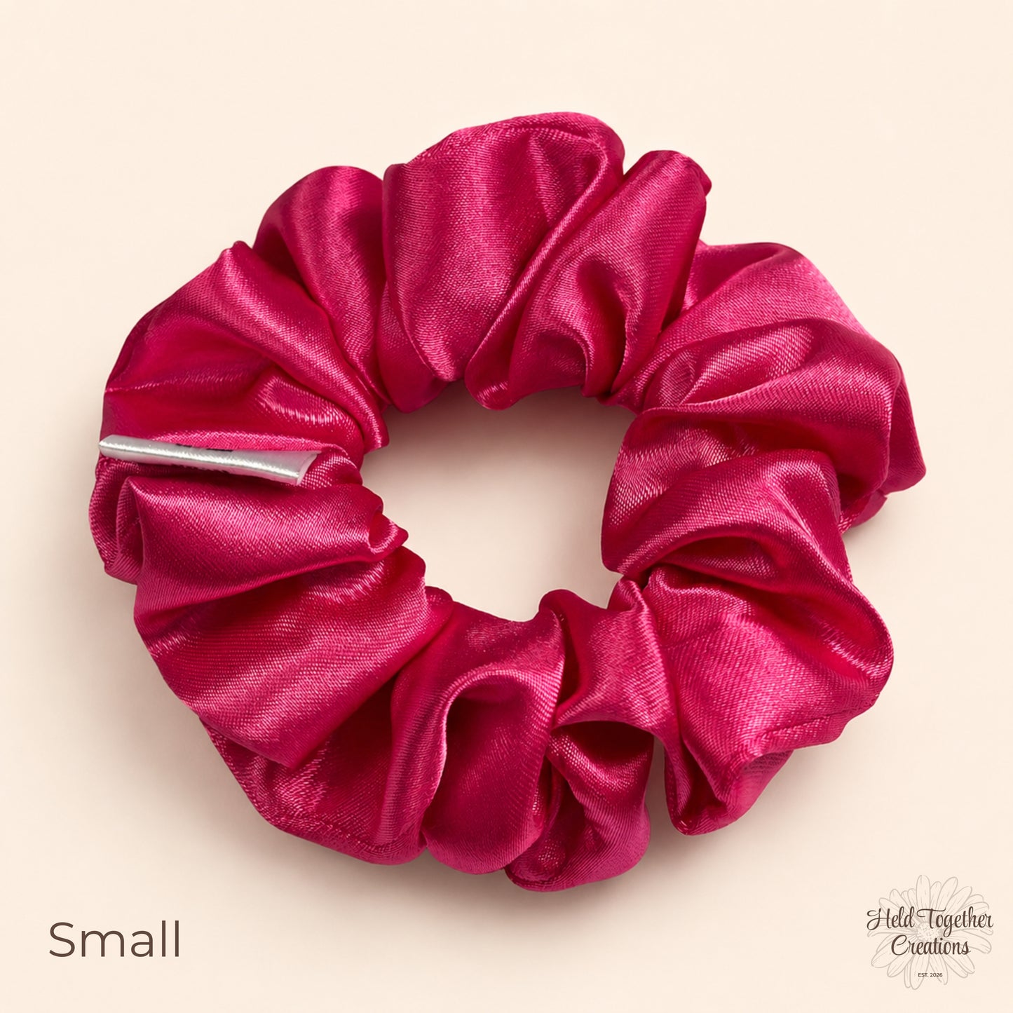Small pink satin scrunchie laid flat showing shiny gathered satin fabric.