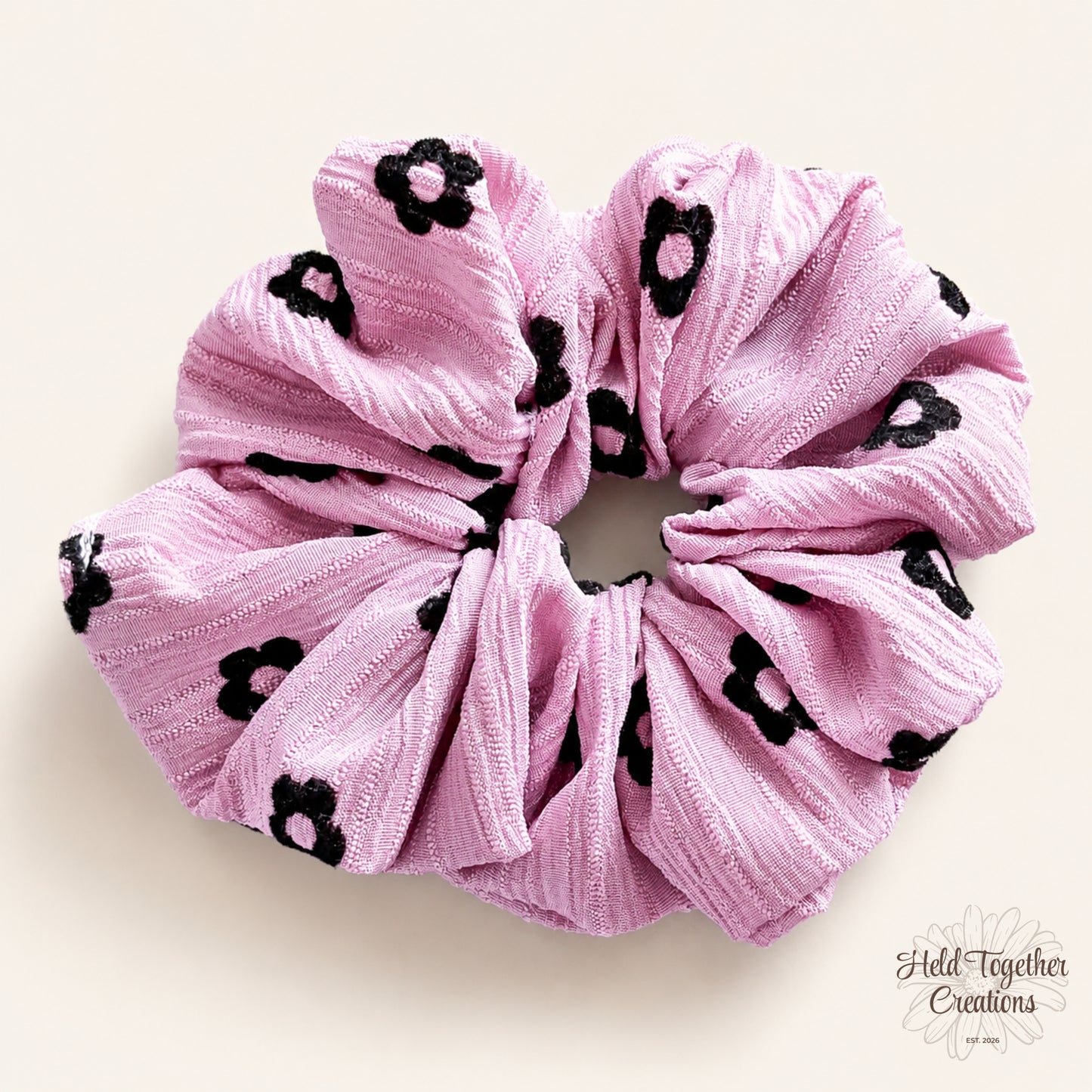 Pink Daisy Charm Scrunchie on warm ivory background showing textured fabric and black daisy print