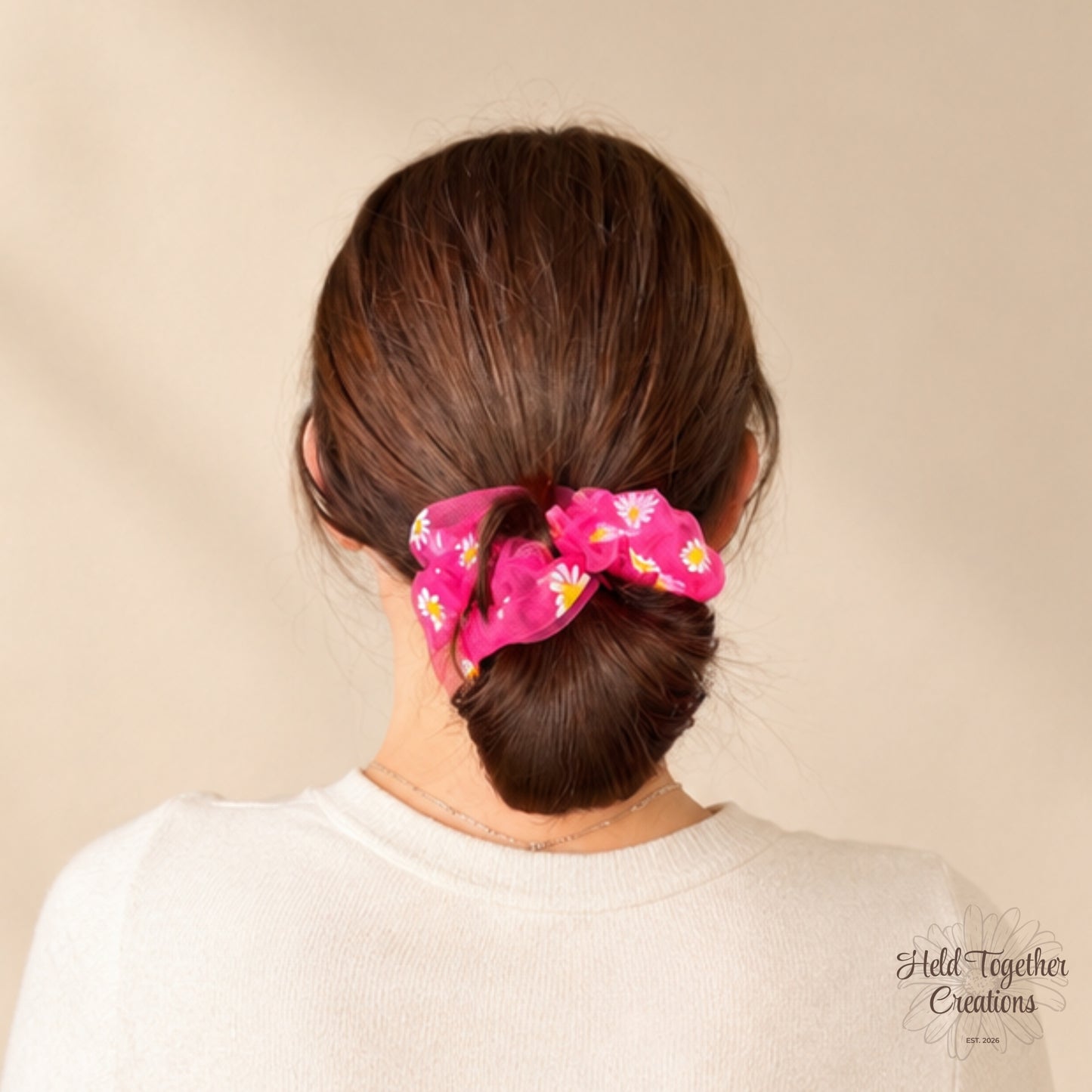Pink daisy puff scrunchie worn around a low bun hairstyle