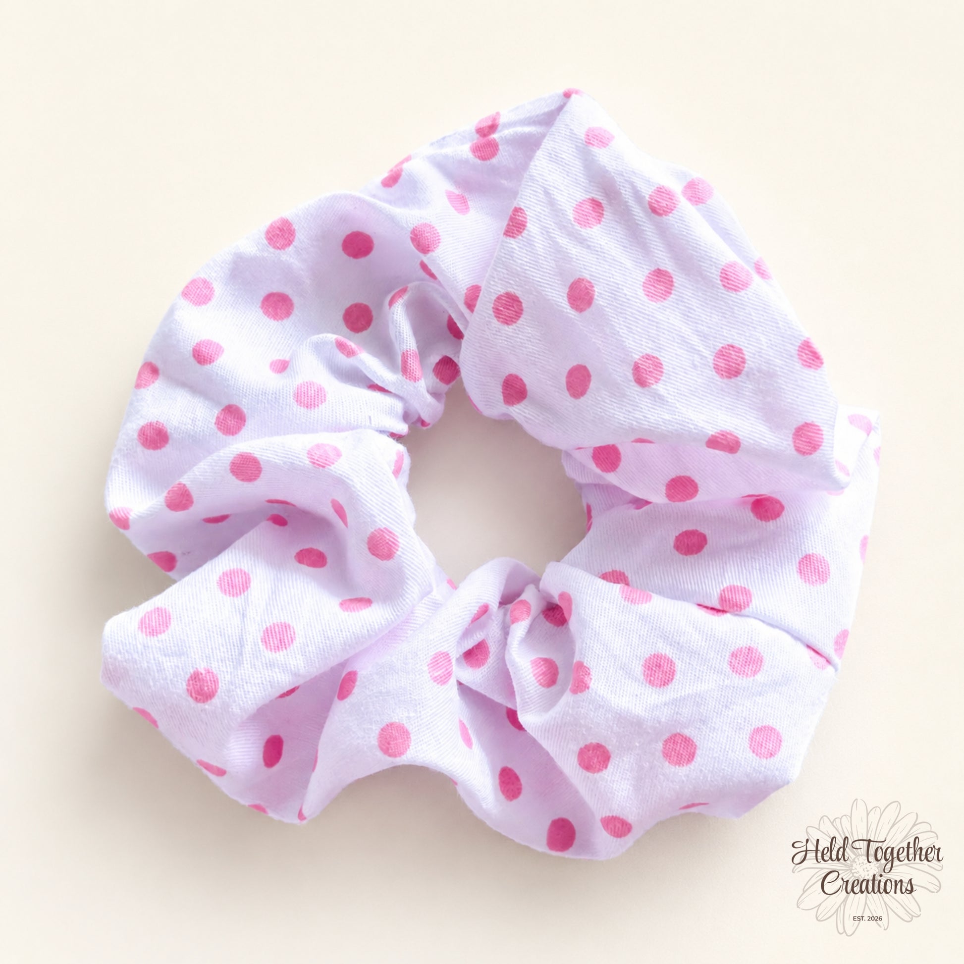 White handmade scrunchie with pink dot print on a soft neutral background.