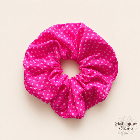 Pink scrunchie with white polka dots on a beige background