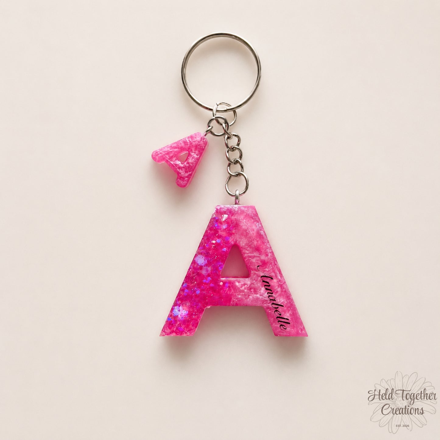 Pink glittery letter 'A' keychain on a beige background
