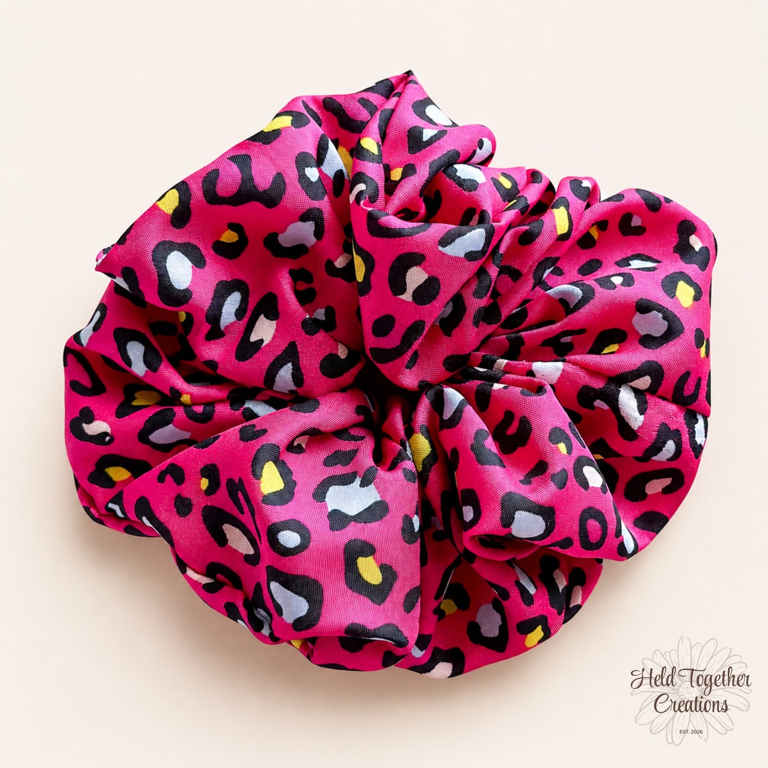 Bright pink leopard print scrunchie on a soft neutral background.