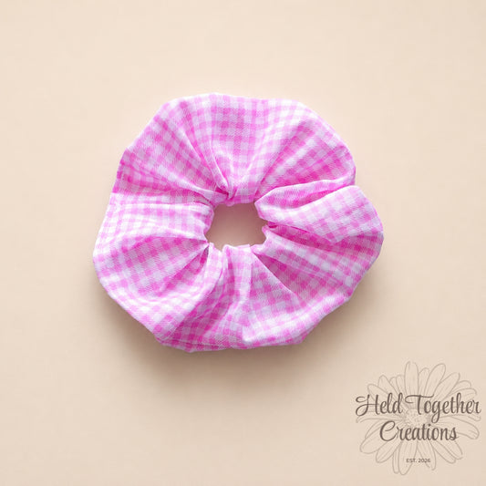Handmade pink and white gingham fabric scrunchie on a soft neutral background.