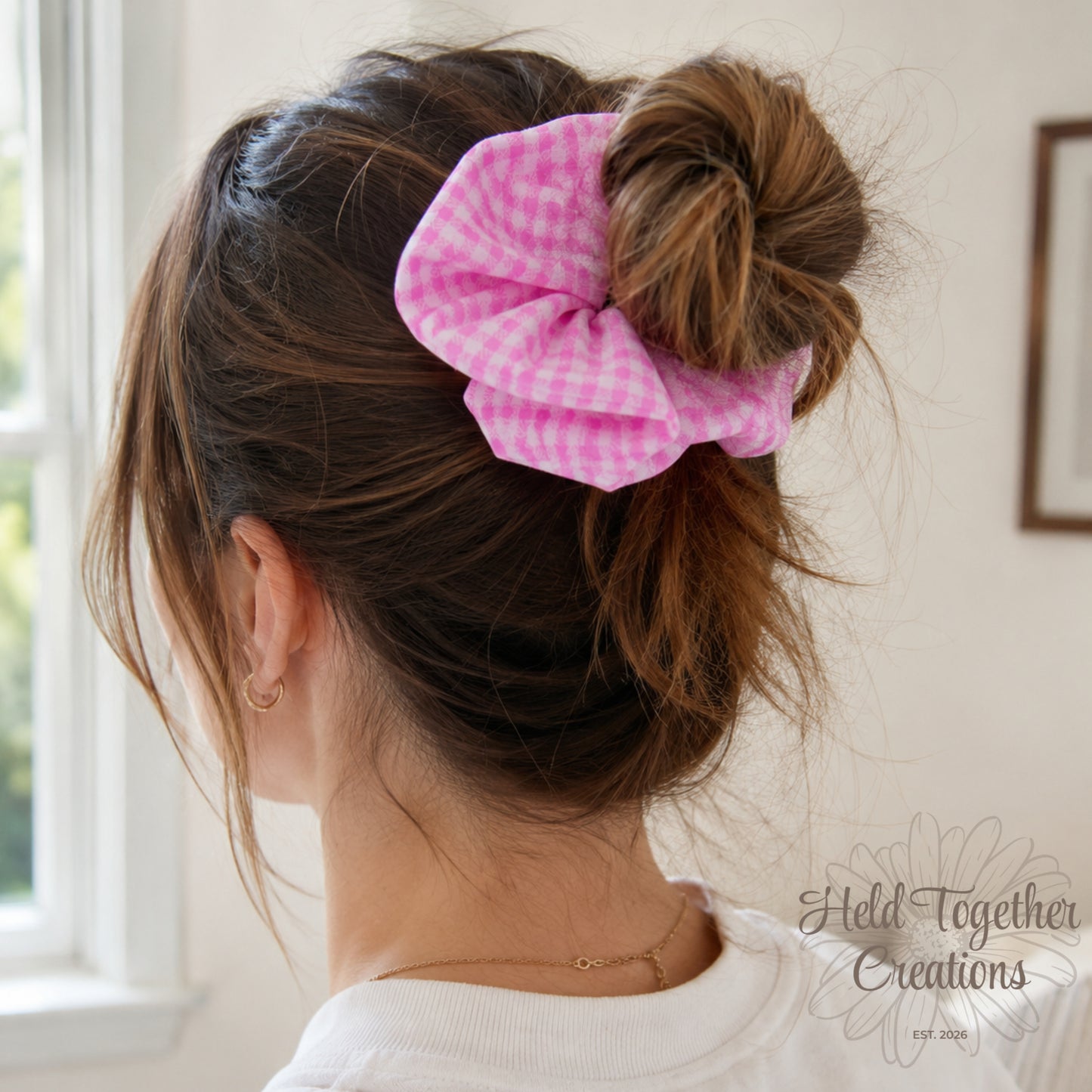 Handmade pink and white gingham fabric scrunchie on a soft neutral background.