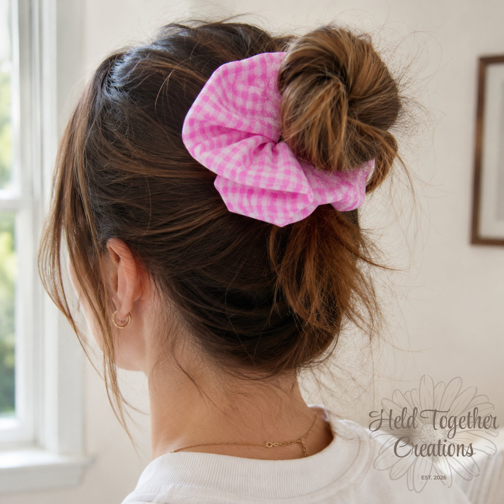 Handmade pink and white gingham fabric scrunchie on a soft neutral background.