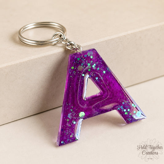 Purple glittery letter 'A' keychain on a beige background