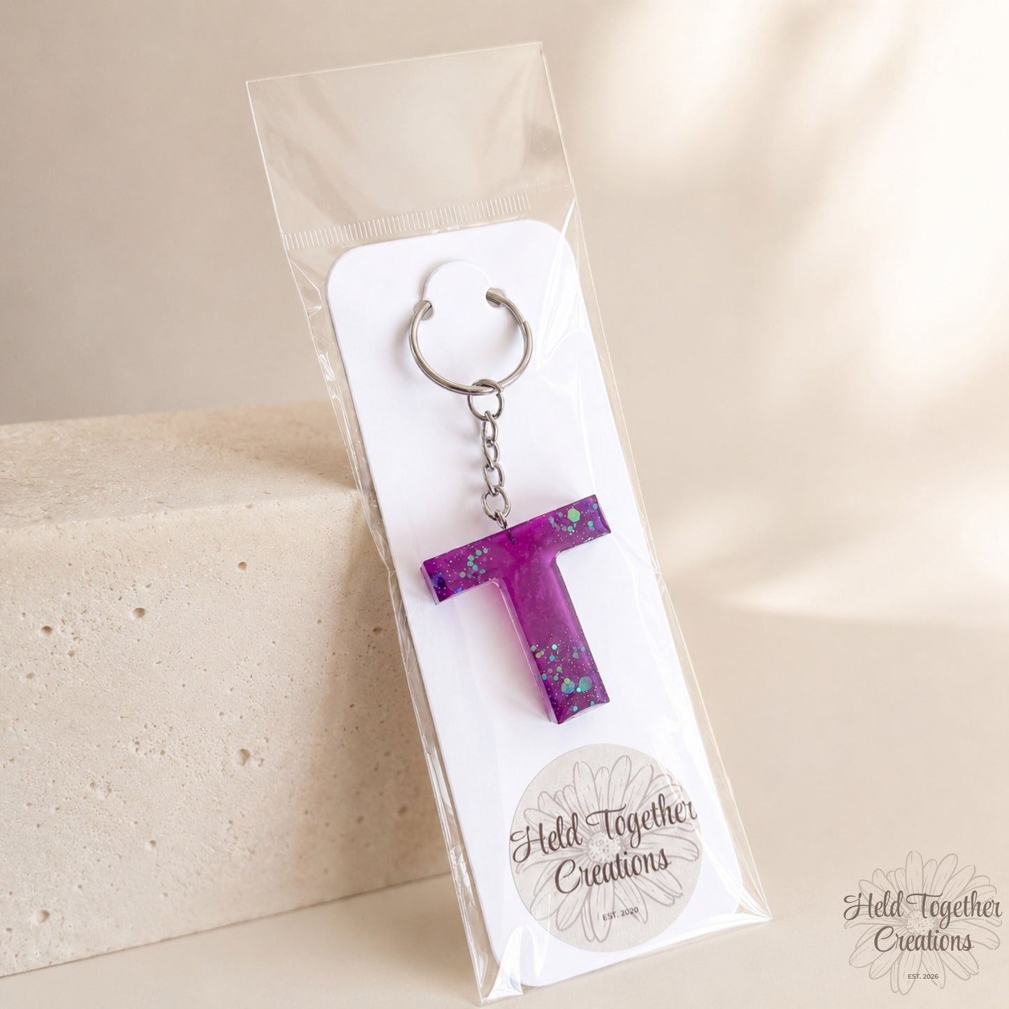 Purple letter 'T' keychain in a clear package with a beige background
