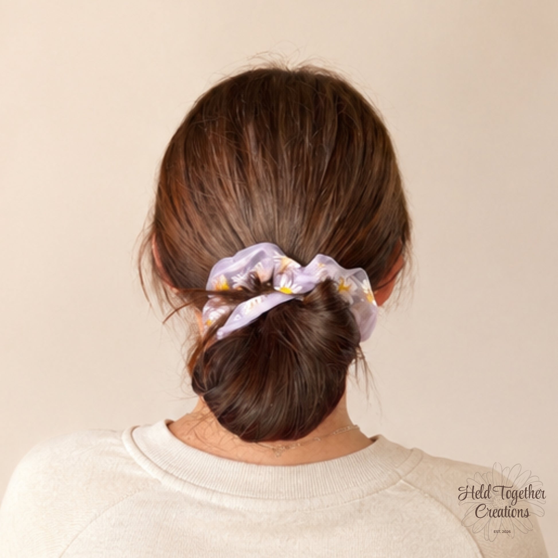 Purple daisy puff scrunchie worn around a low bun hairstyle