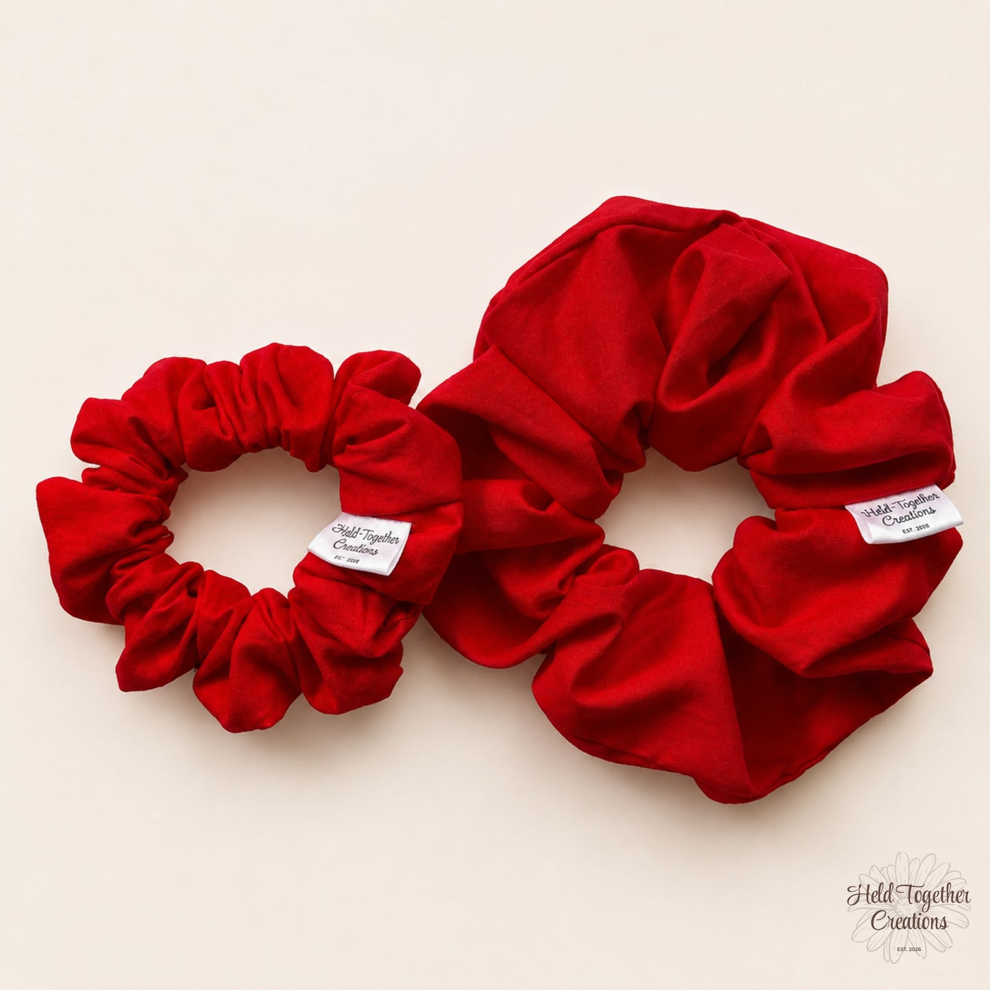 Small and large red cotton scrunchies displayed together on a warm ivory background.
