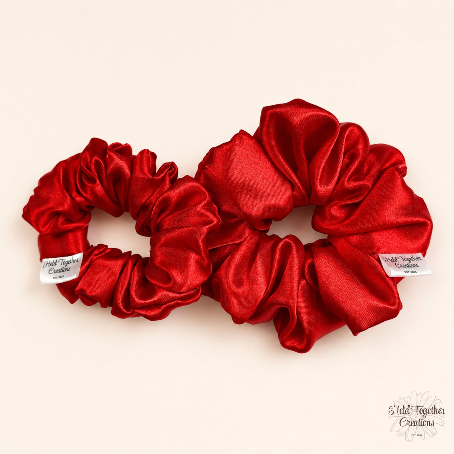 Small and large red satin scrunchies shown together on warm ivory background