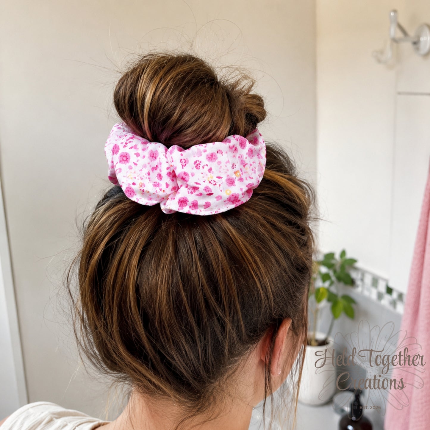 Person with a bun wearing a pink floral scrunchie, with 'Held Together Creations' branding.