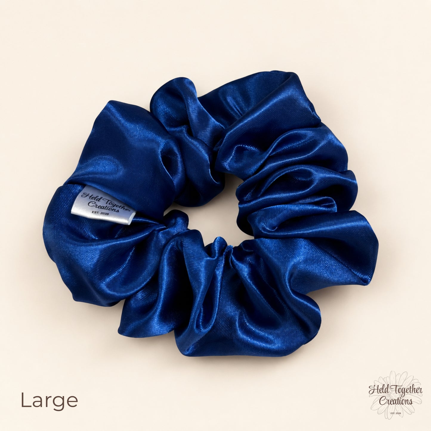 Large royal blue satin scrunchie laid flat showing glossy gathered fabric and brand tag.
