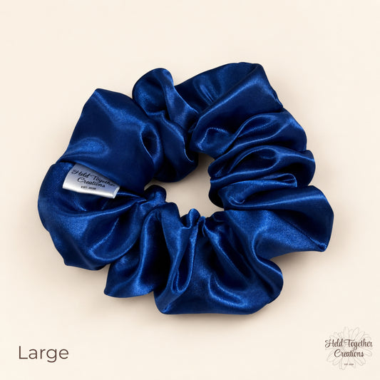Large royal blue satin scrunchie laid flat showing glossy gathered fabric and brand tag.