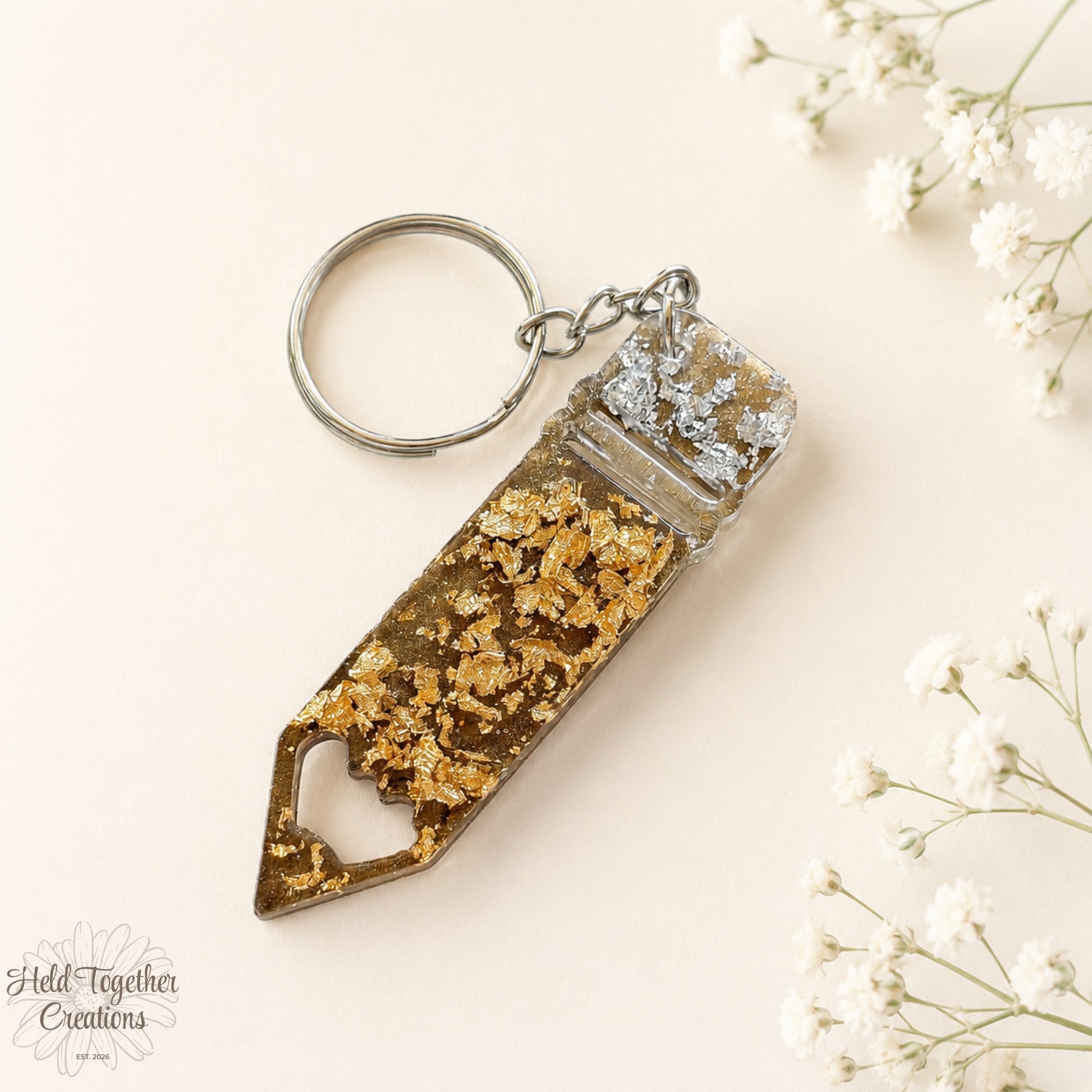 Handmade pencil-shaped resin keyring with gold and silver flakes and metal keyring hardware on a soft neutral background.
