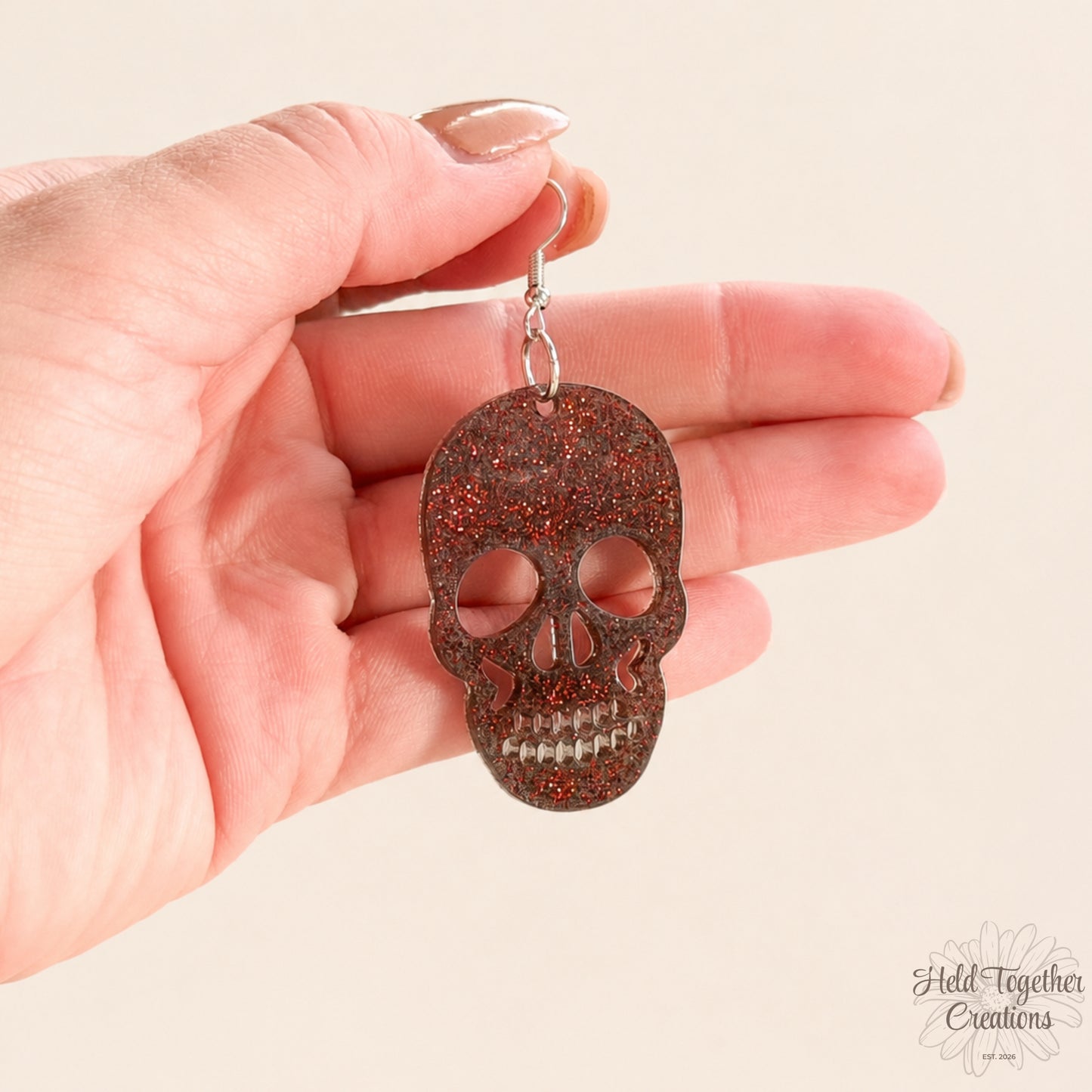 Skull-shaped earring held in a hand against a beige background