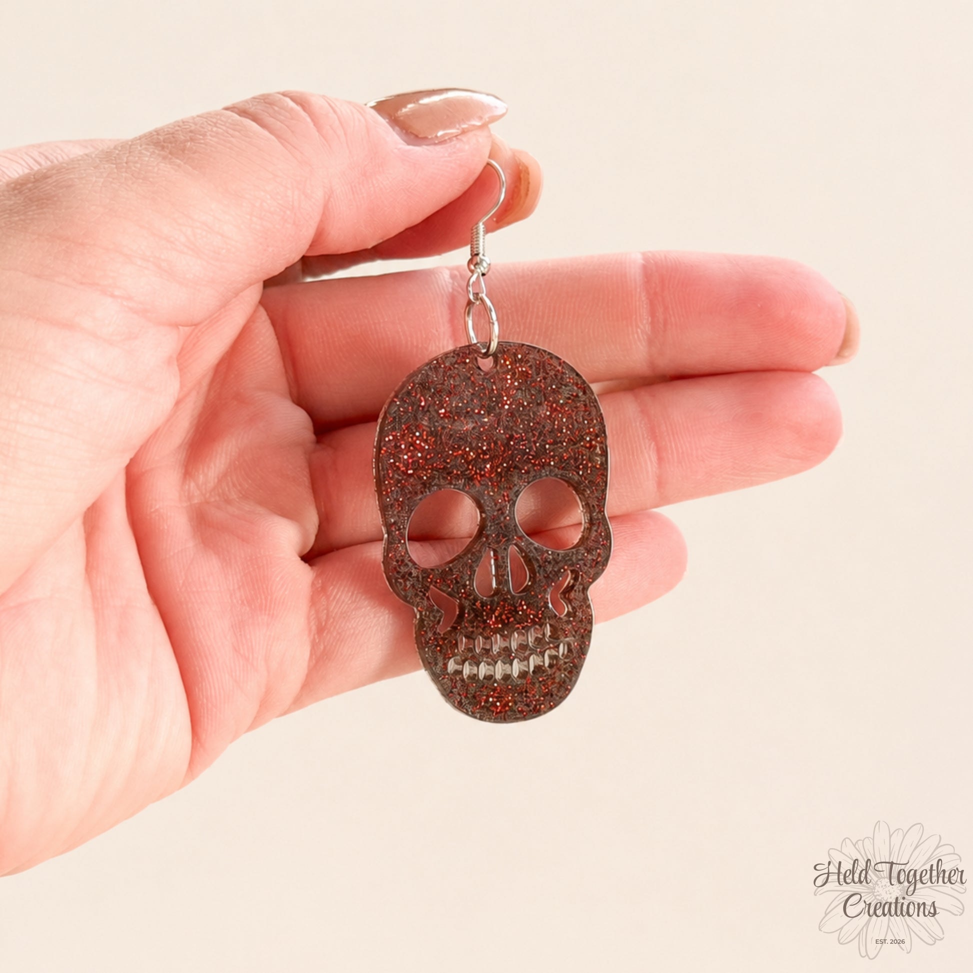Skull-shaped earring held in a hand against a beige background