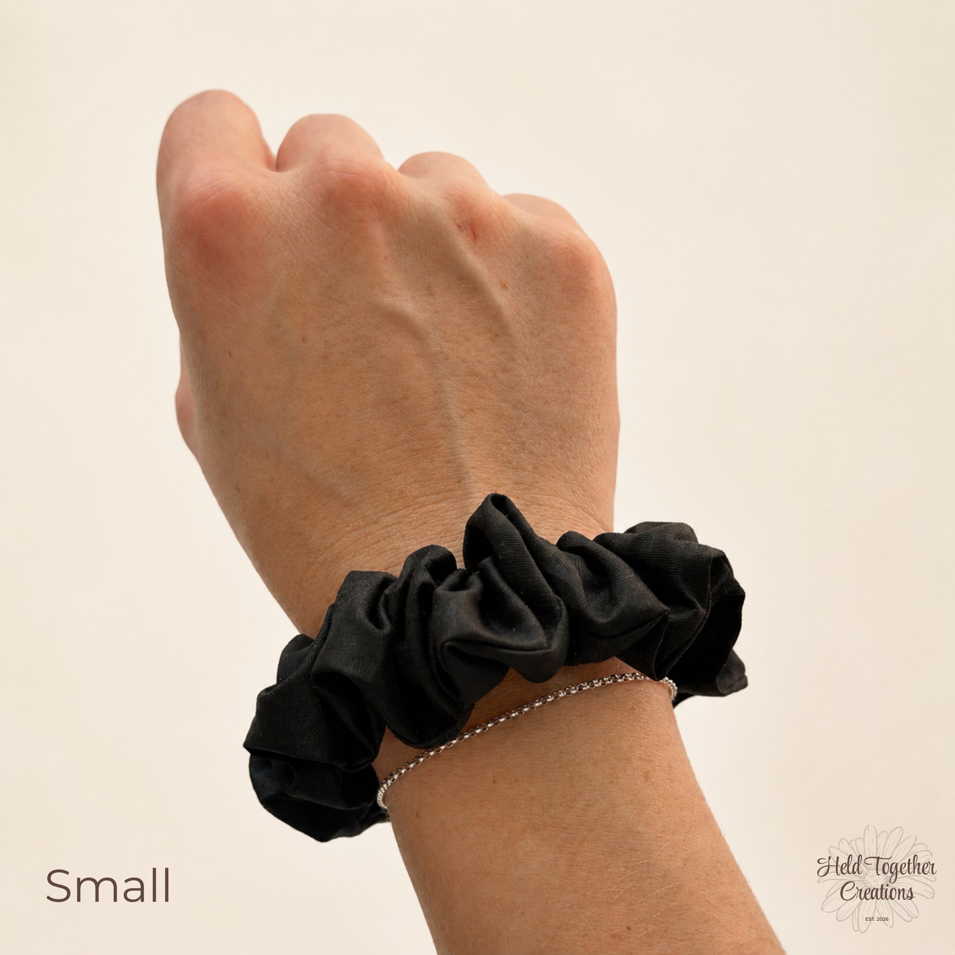 A black cotton scrunchie worn on a person's wrist, shown against a plain light beige background. The text 'Small' appears in the lower left, and a brand watermark 'Hold Together Creations' is visible in the lower right.