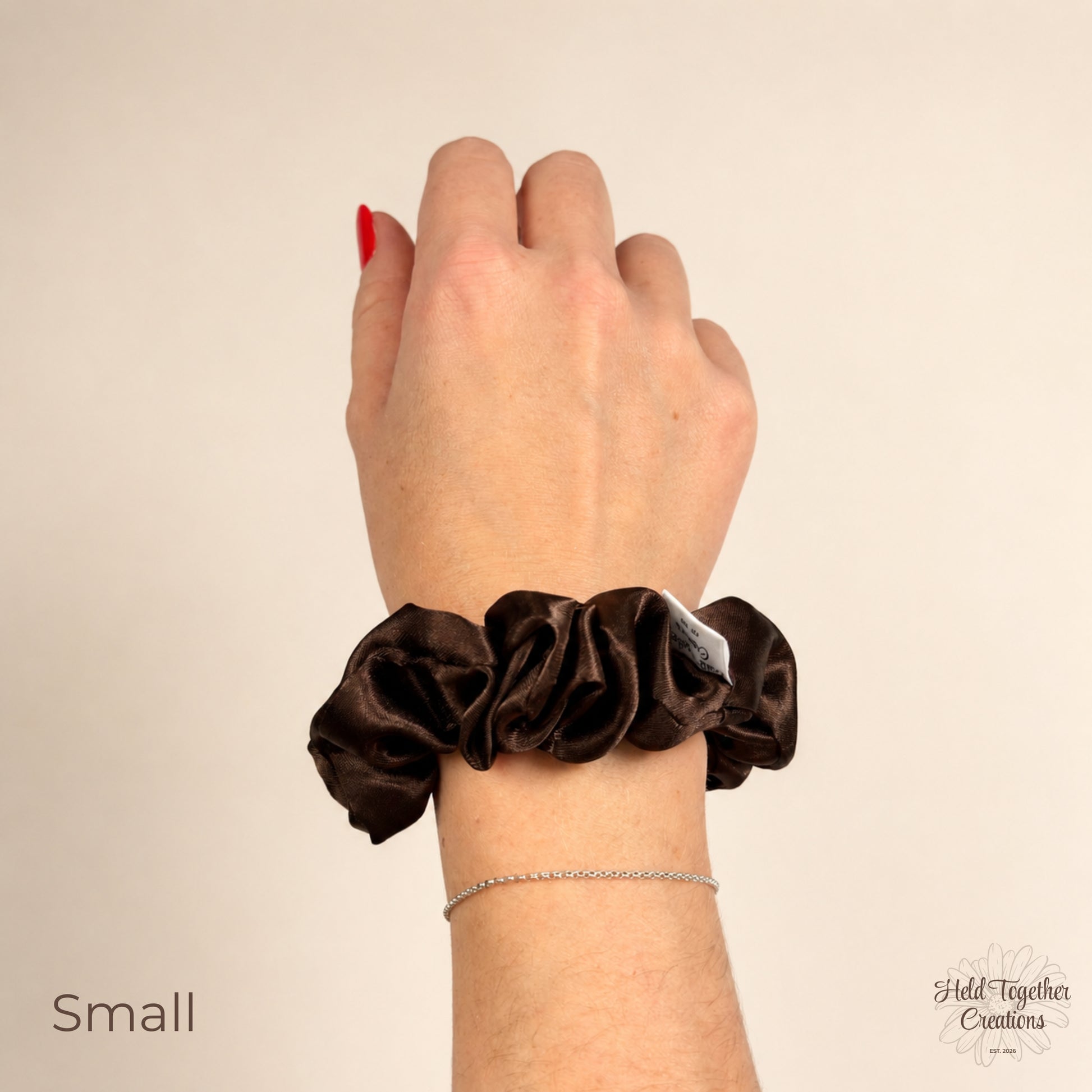 Small brown satin scrunchie worn on wrist showing compact gathered satin fabric and rich chocolate brown colour.
