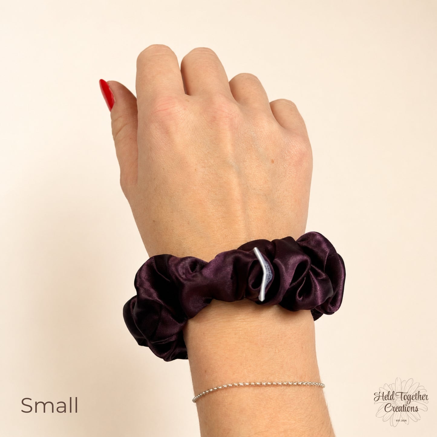 Small deep plum satin scrunchie worn on wrist showing rich plum satin fabric