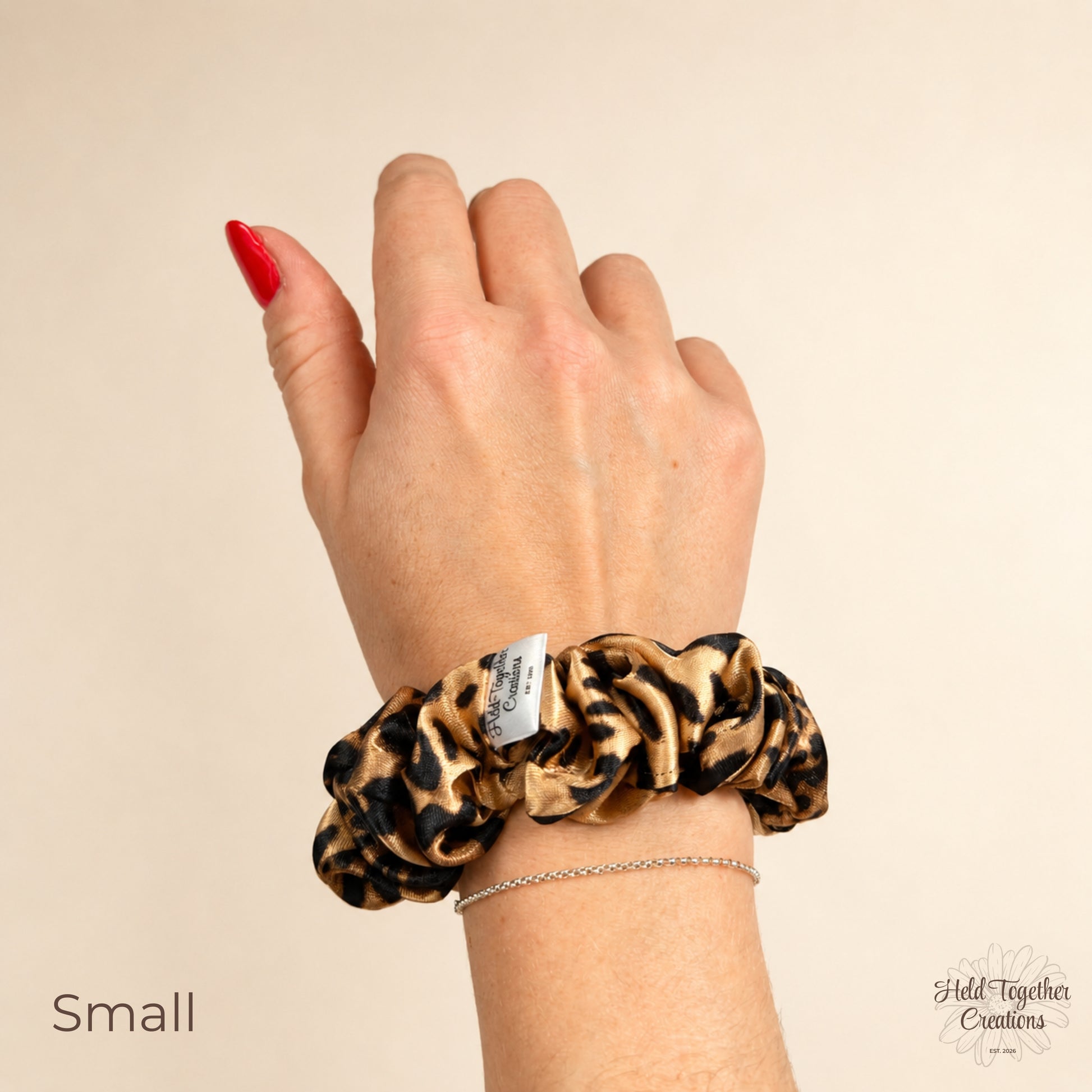 Small leopard satin scrunchie worn on the wrist, showing the size and glossy satin finish.