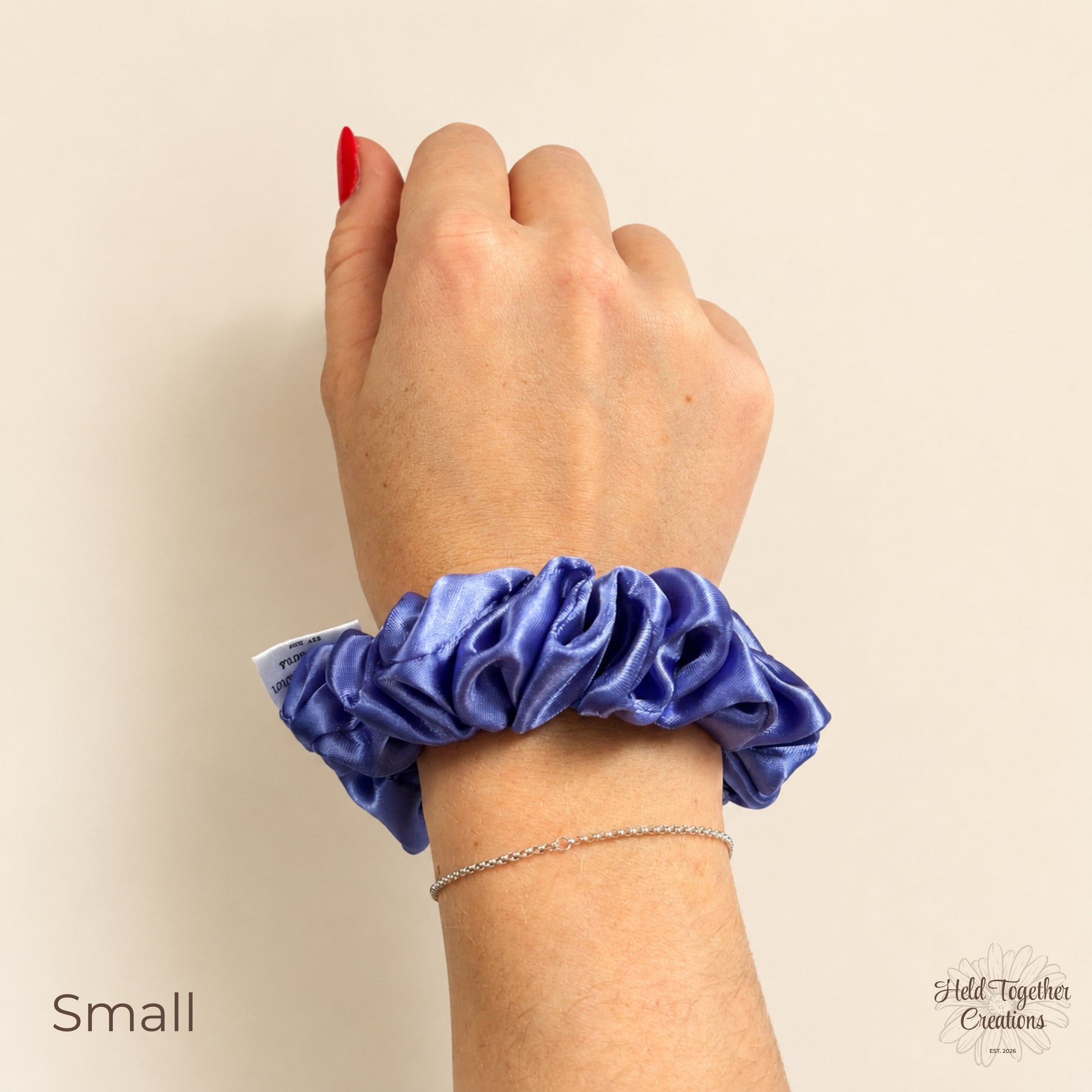 Small lilac satin scrunchie worn on wrist against a warm ivory background.