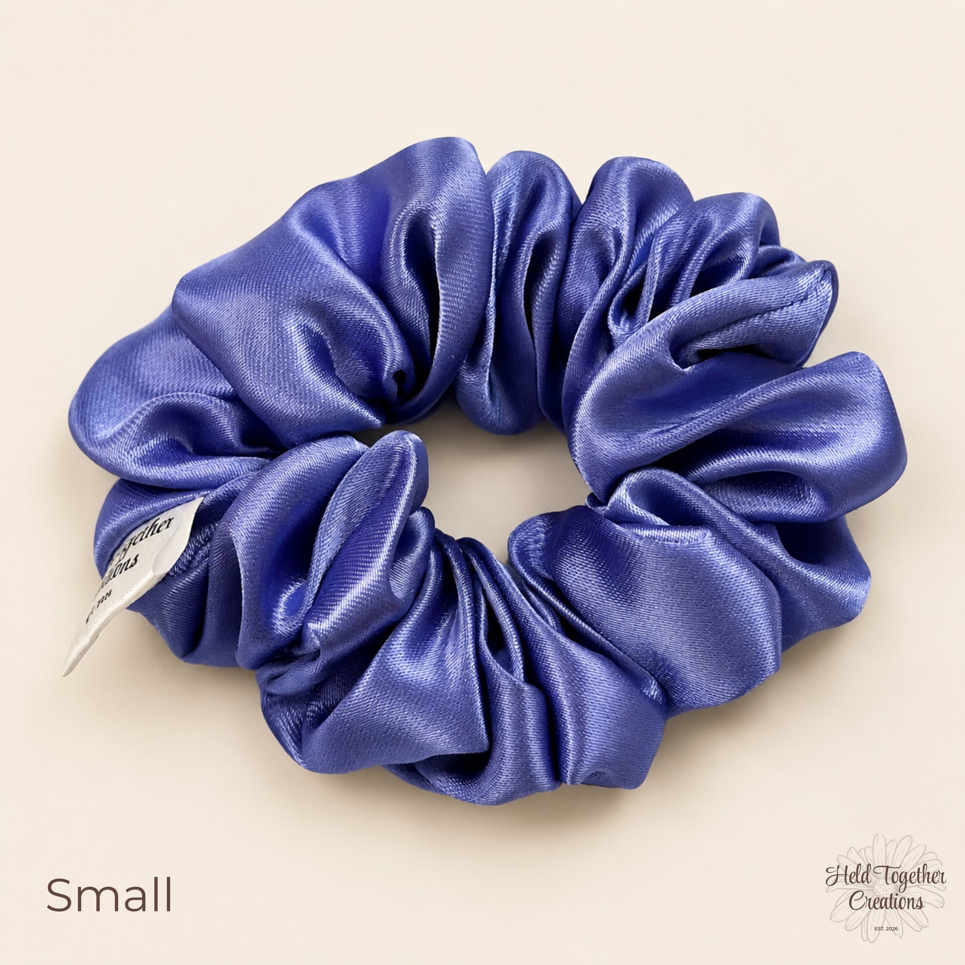Small lilac satin scrunchie laid flat showing shiny gathered satin fabric.