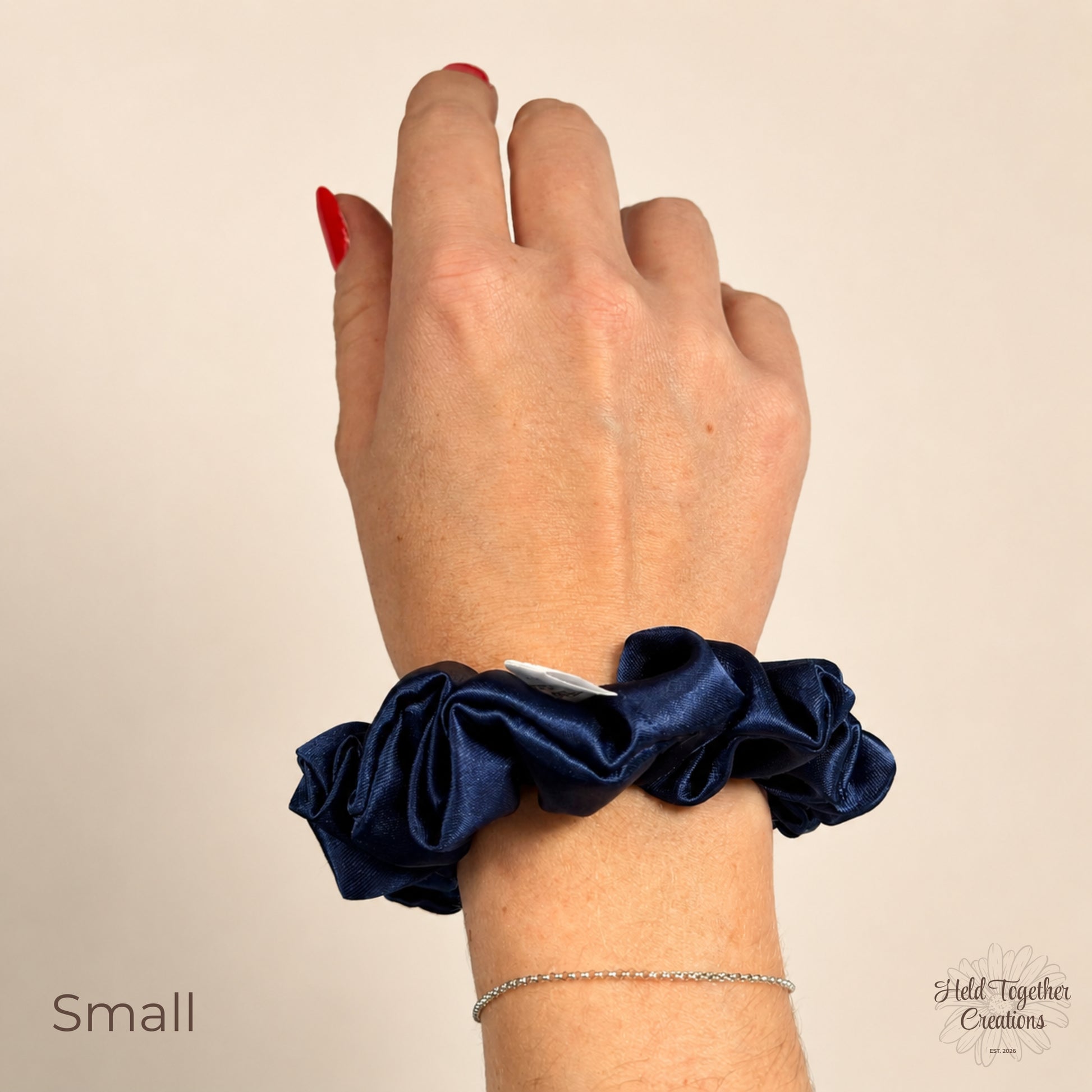 Small navy satin scrunchie worn on wrist to show size and shiny satin texture.