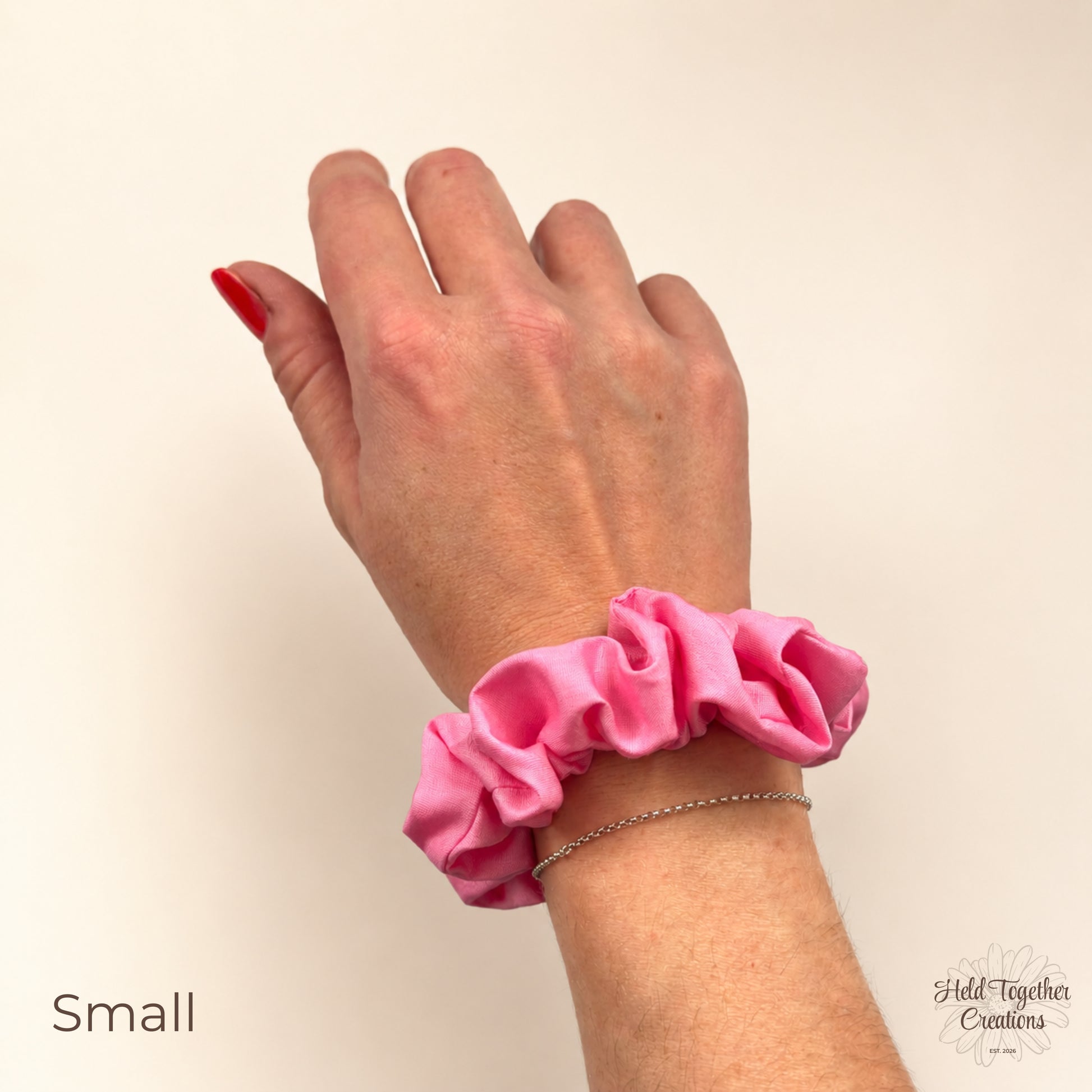 Small pink cotton scrunchie worn on wrist against a neutral background