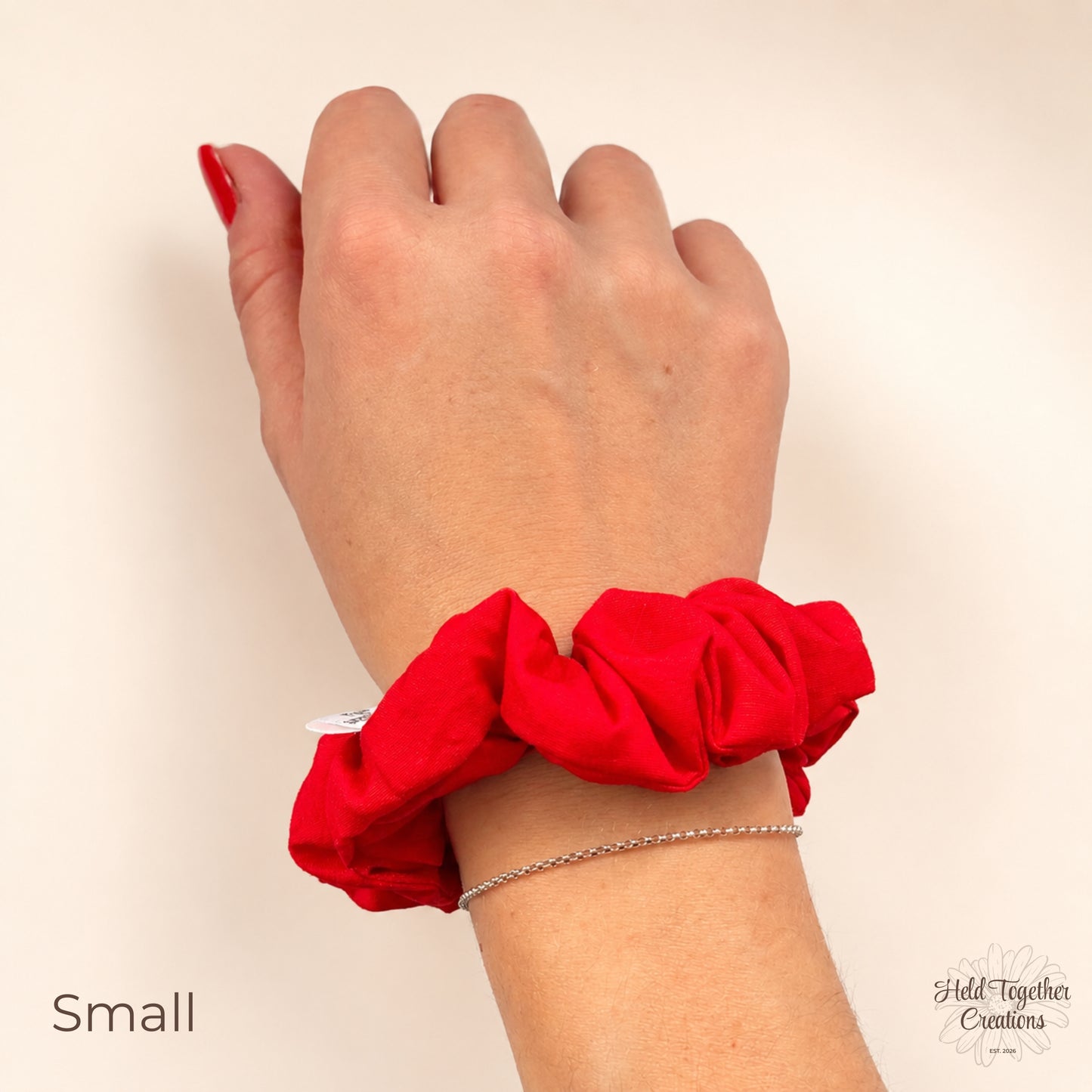 Small red cotton scrunchie worn on wrist against a warm ivory background.