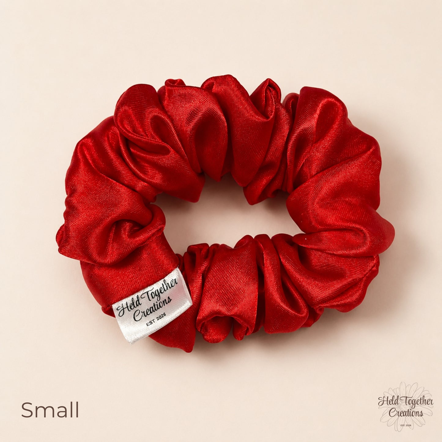 Small red satin scrunchie on warm ivory background with branded tag