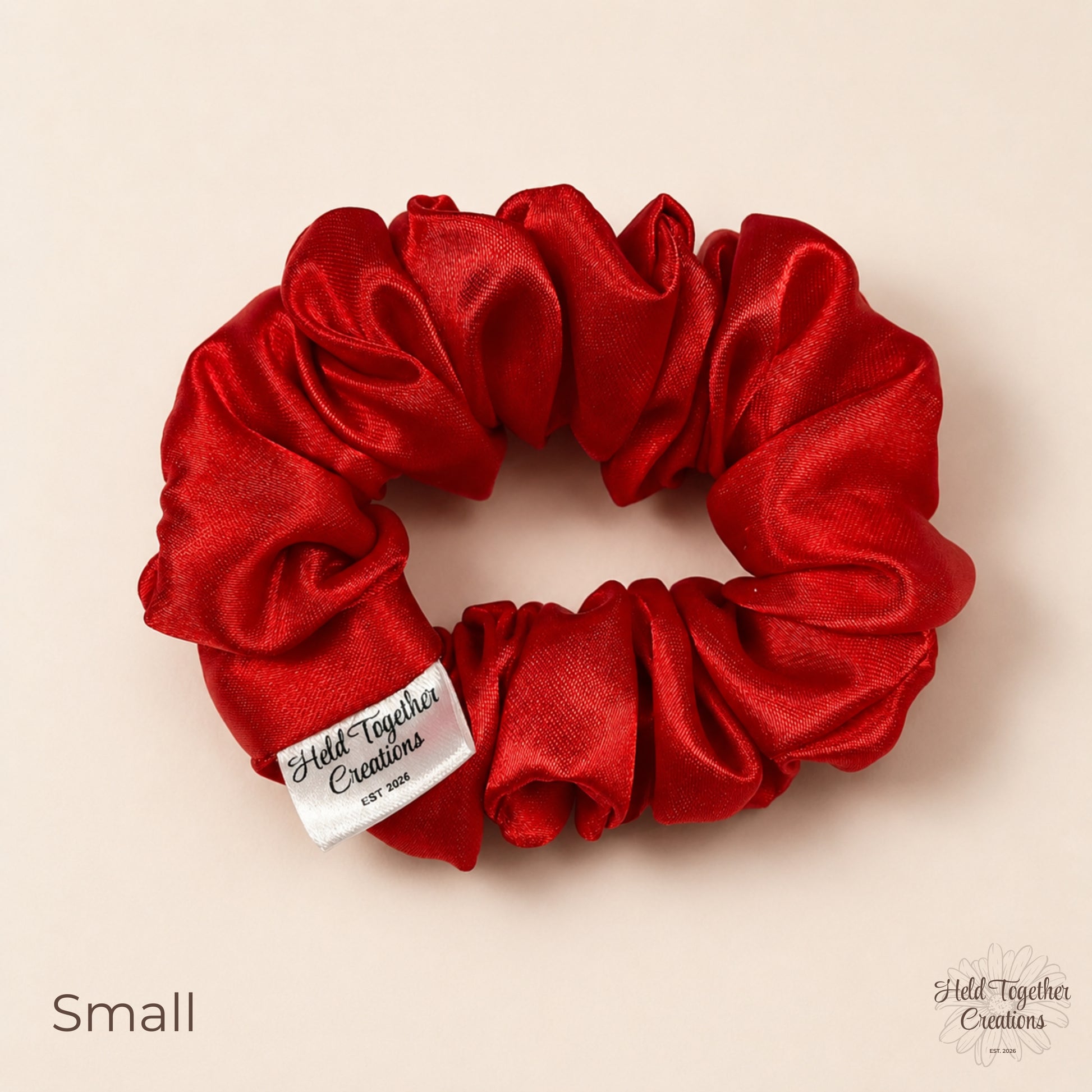 Small red satin scrunchie on warm ivory background with branded tag