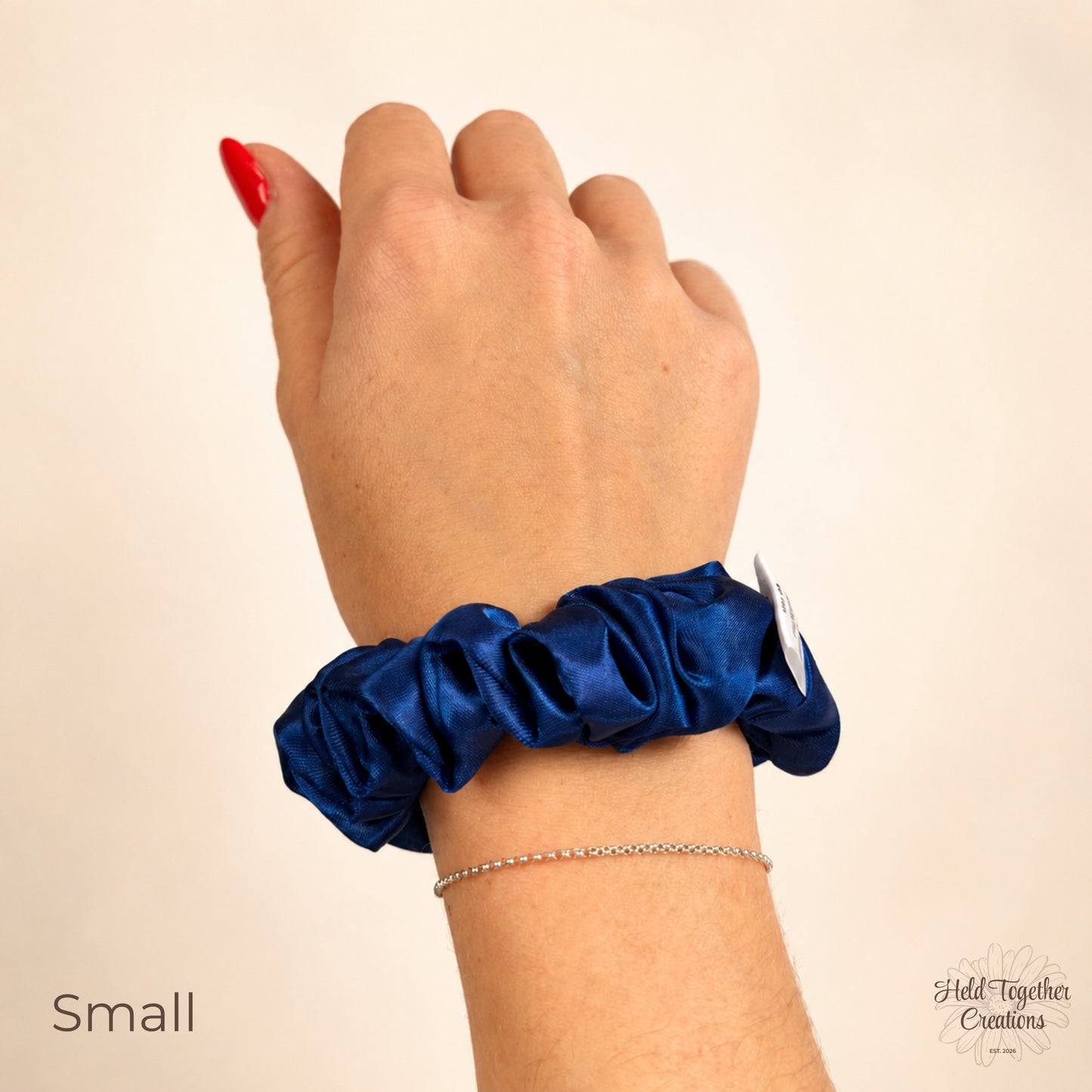 Small royal blue satin scrunchie worn around the wrist on a warm ivory background.