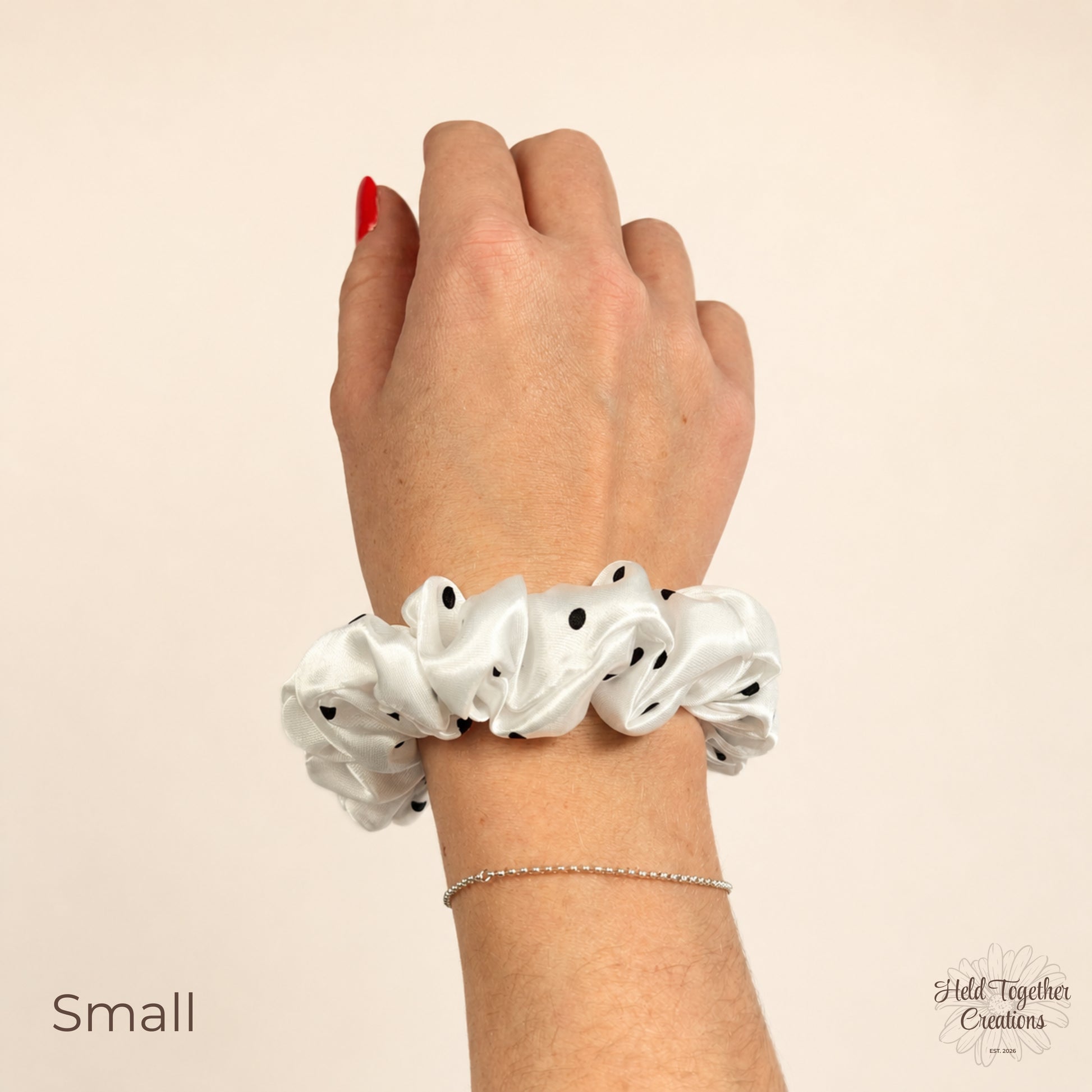 Small white satin scrunchie with black polka dots worn on wrist.