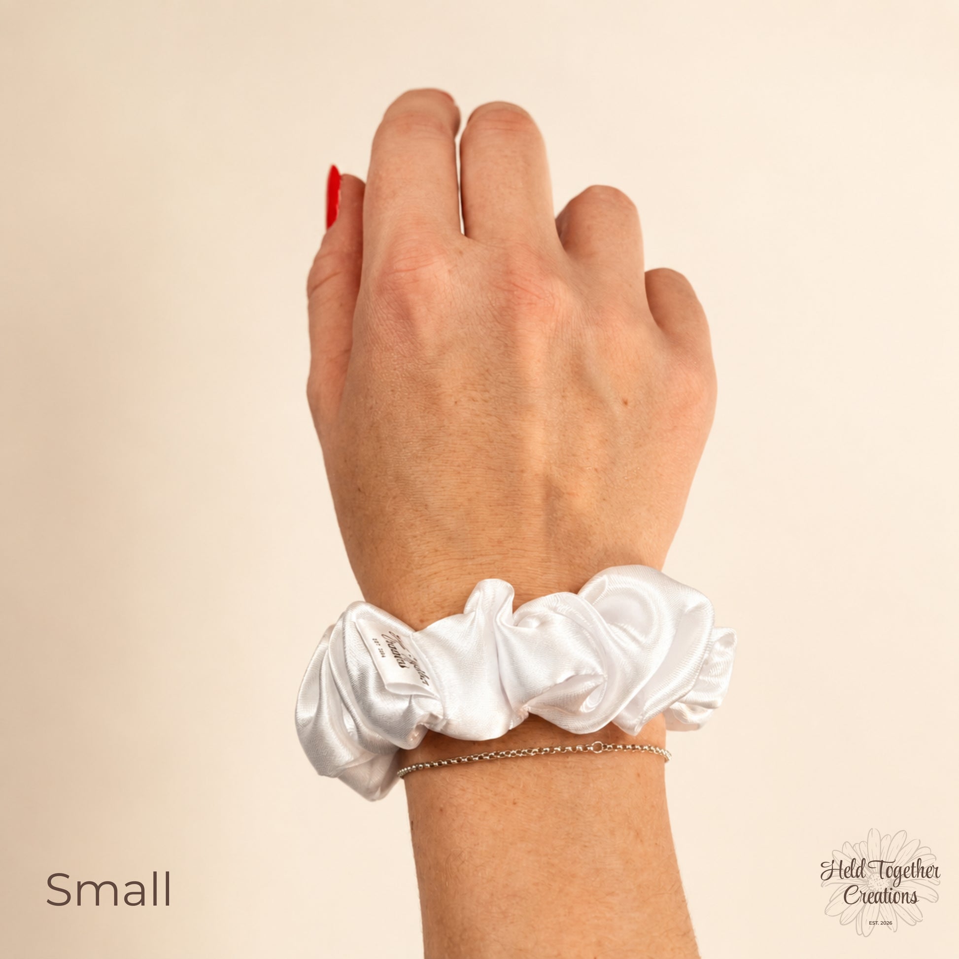 Small white satin scrunchie worn on wrist, showing the smooth satin finish and handmade label.