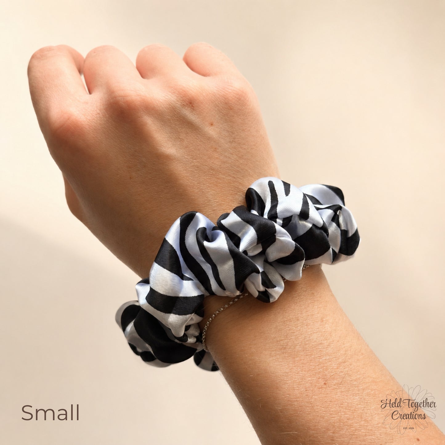 A black and white zebra-print fabric scrunchie worn on a person's wrist, shown against a plain beige background with the text 'Small' in the lower left corner.