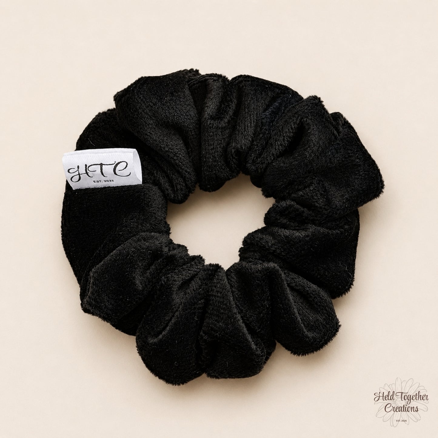 Black velvet handmade scrunchie with white HTC label on a warm neutral background.