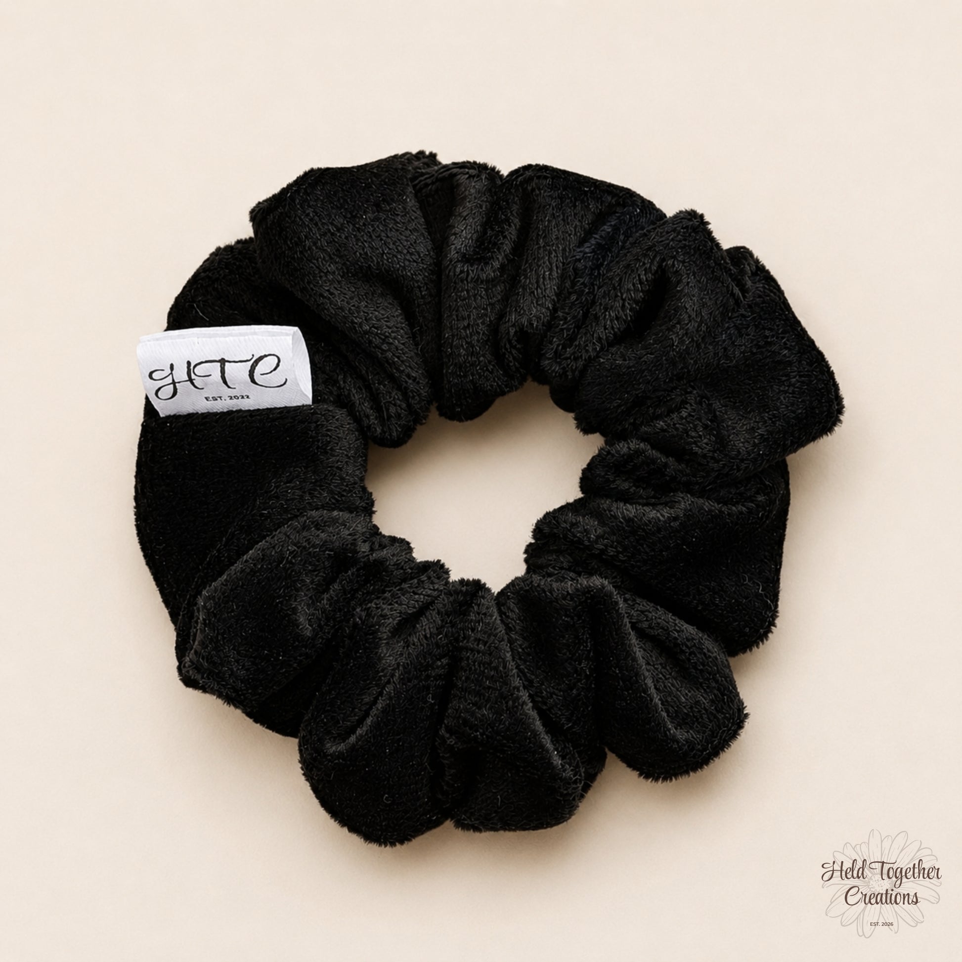 Black velvet handmade scrunchie with white HTC label on a warm neutral background.