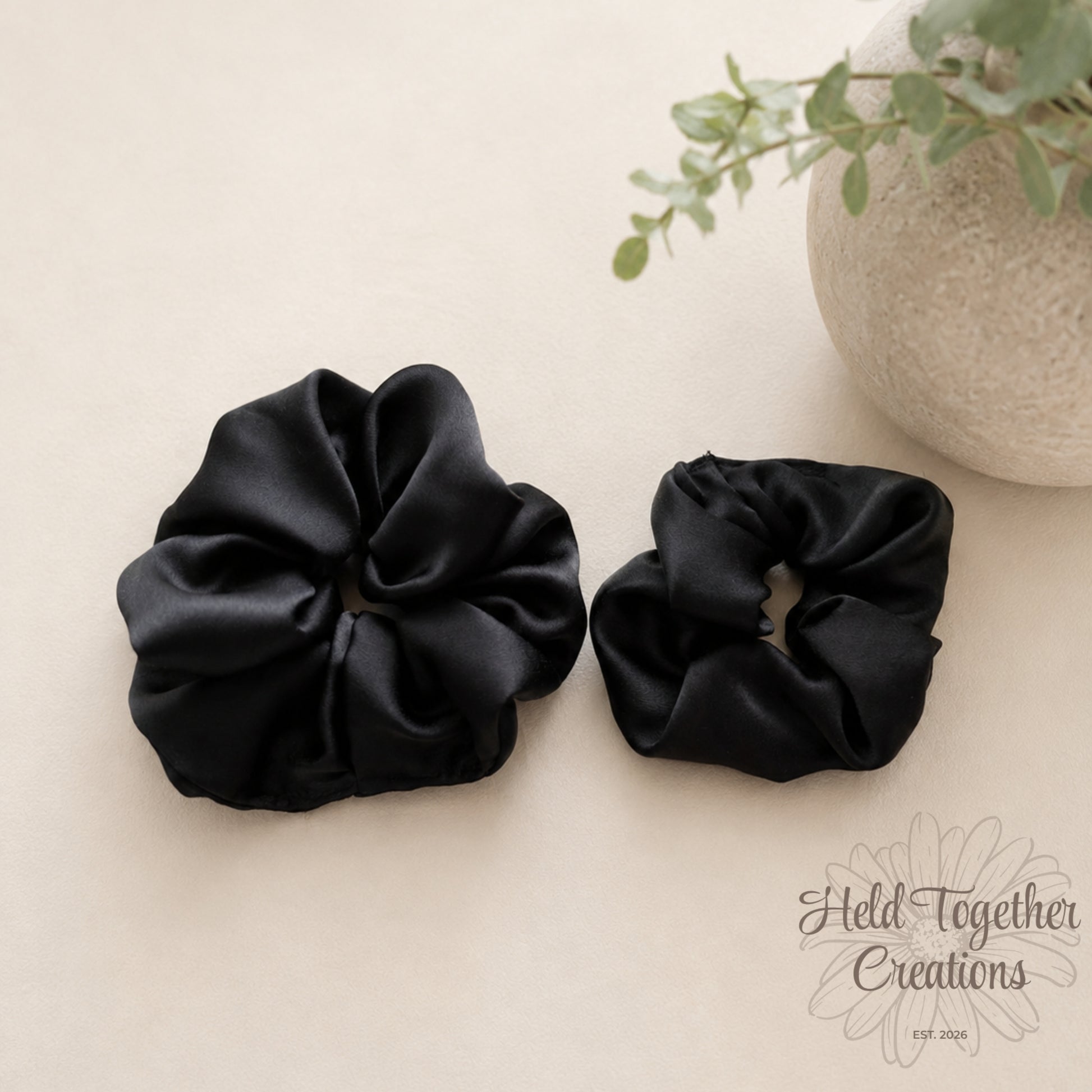 Black satin handmade scrunchies in large and small sizes on a soft neutral background.