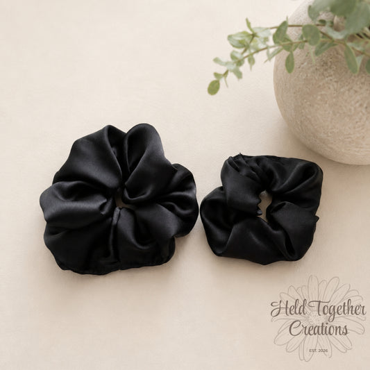 Black satin handmade scrunchies in large and small sizes on a soft neutral background.