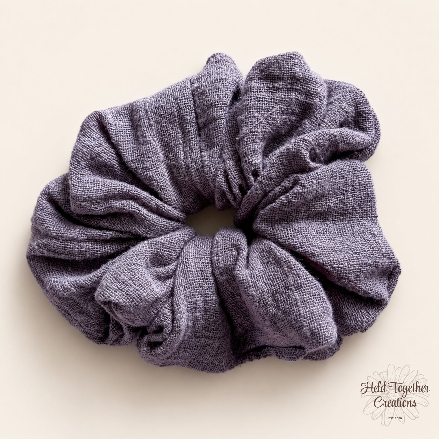 Handmade Storm Linen Scrunchie in textured grey-purple fabric on a warm ivory background.