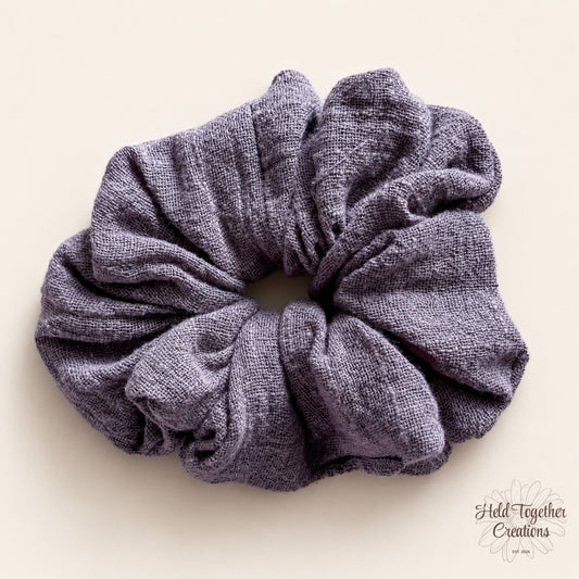 Handmade Storm Linen Scrunchie in textured grey-purple fabric on a warm ivory background.