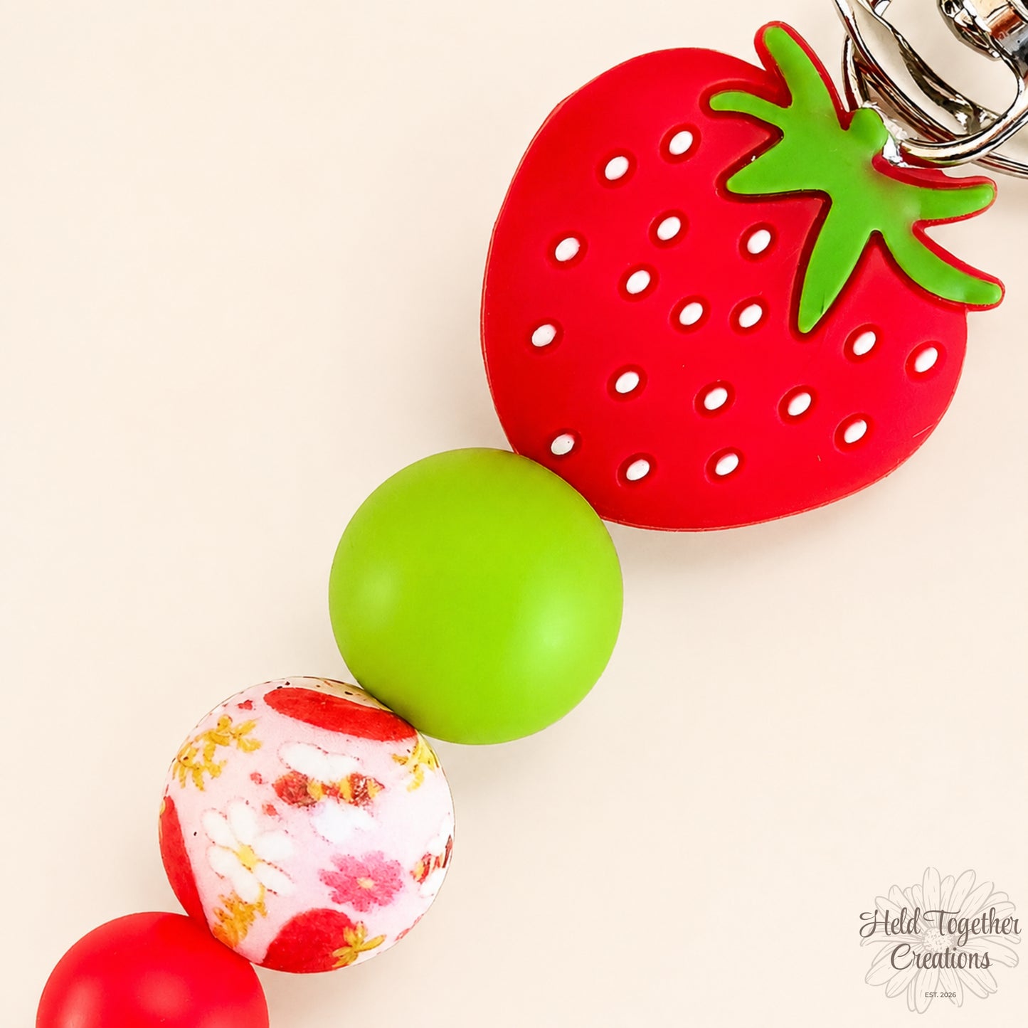 Strawberry-shaped keychain with a green ball and floral-patterned ball on a beige background