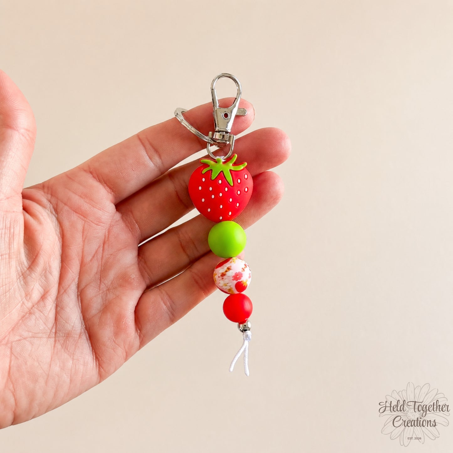 Hand holding a keychain with strawberry-shaped beads against a beige background