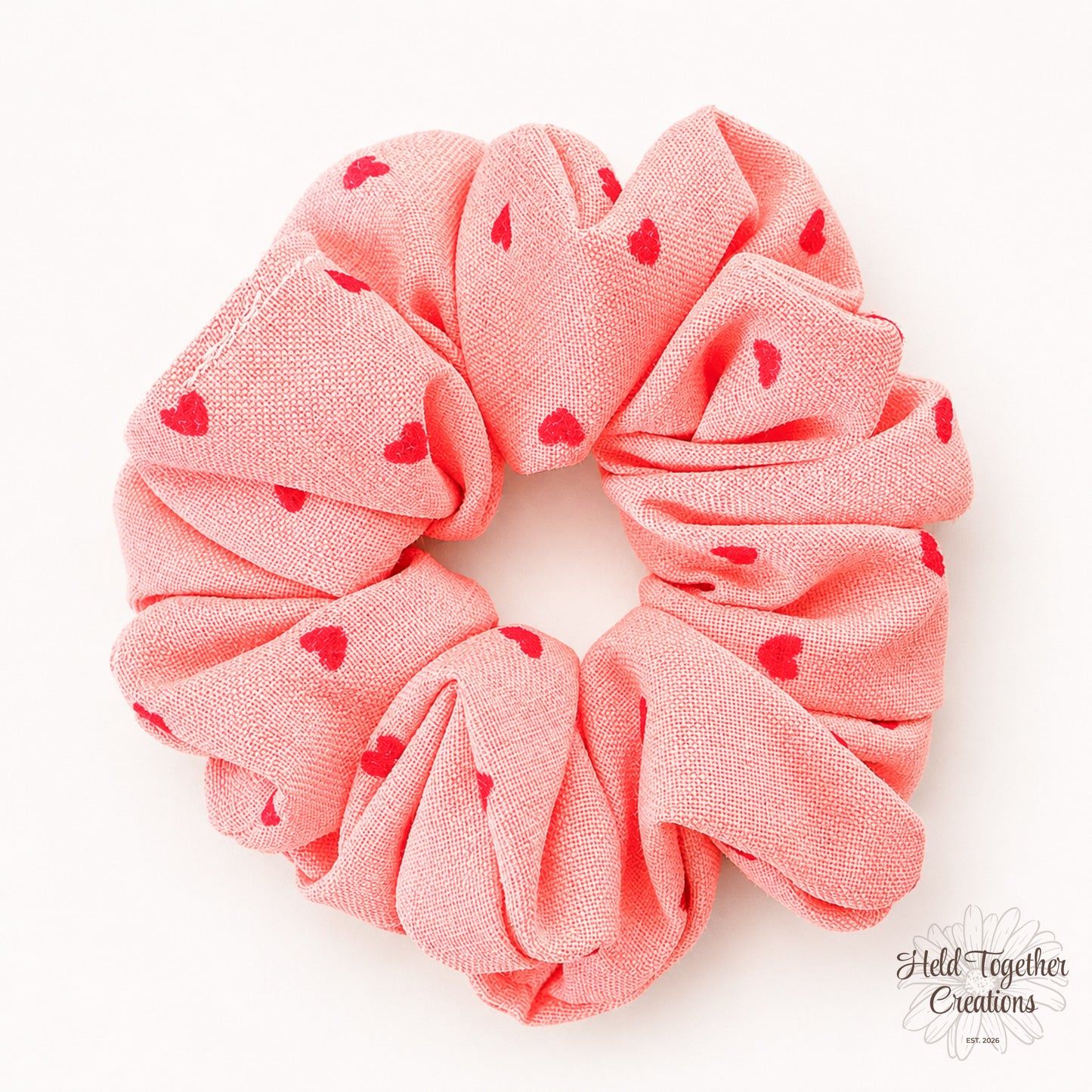 Coral velvet-style scrunchie with red heart print on a warm ivory background.