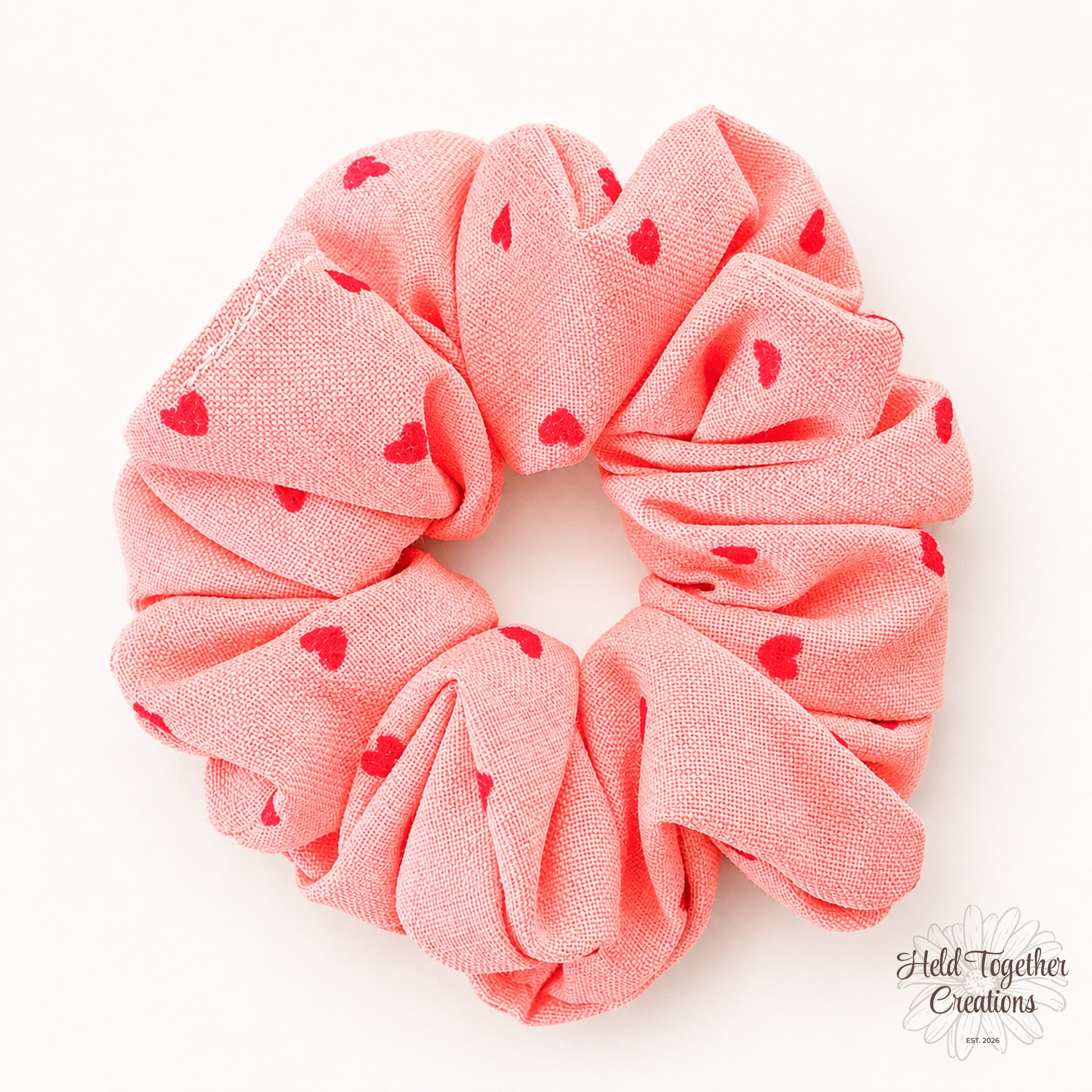 Coral velvet-style scrunchie with red heart print on a warm ivory background.