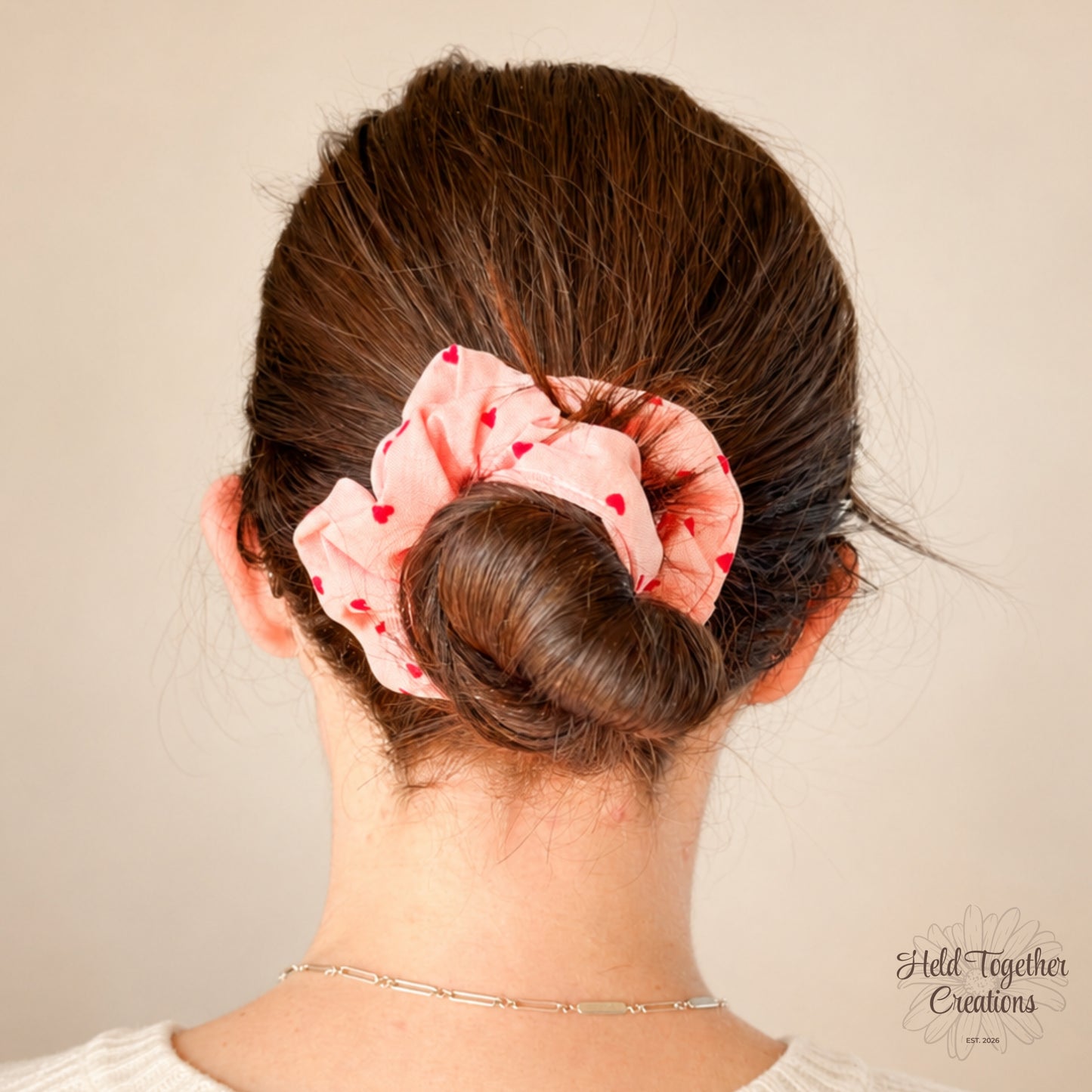 Coral velvet-style scrunchie with red heart print on a warm ivory background.