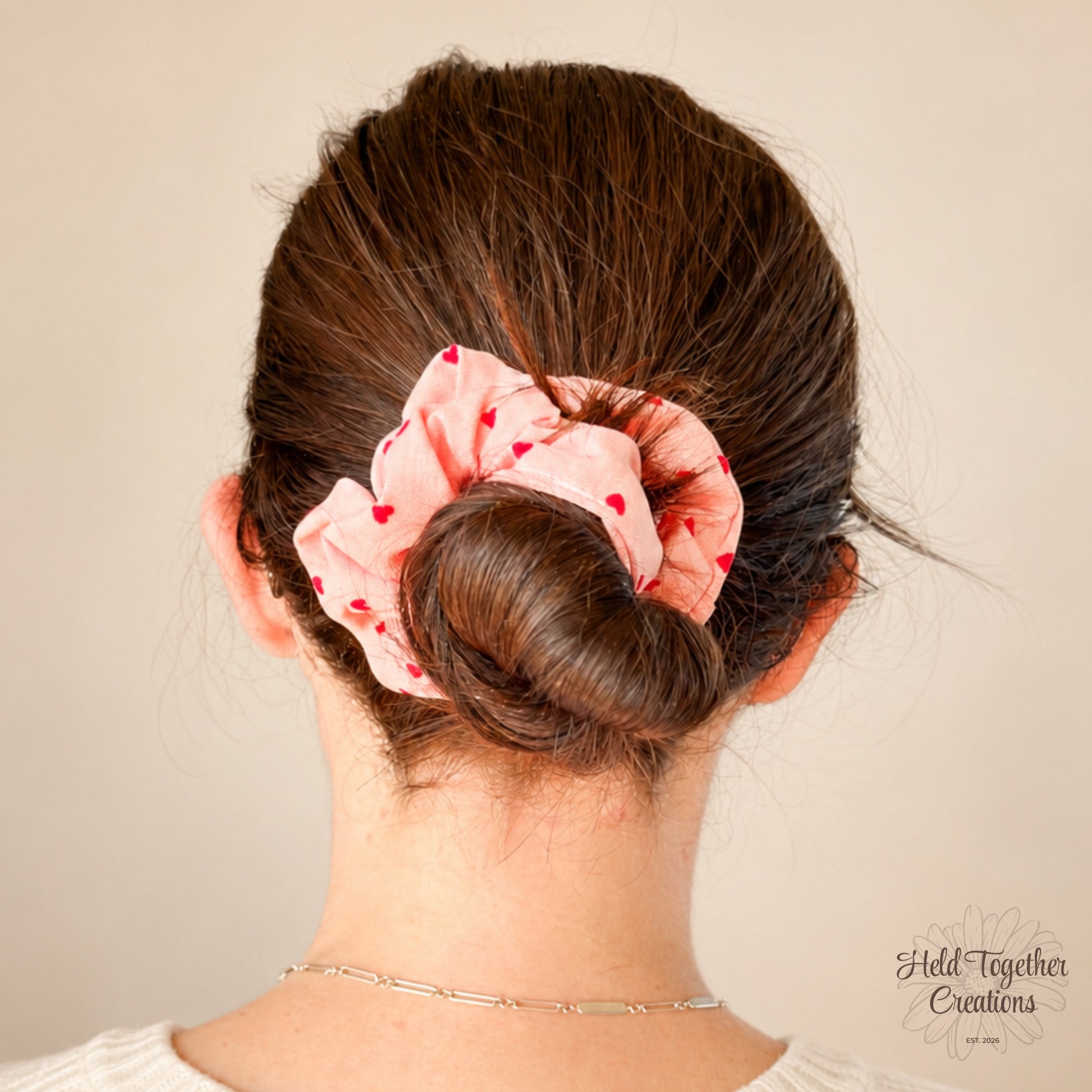 Coral velvet-style scrunchie with red heart print on a warm ivory background.