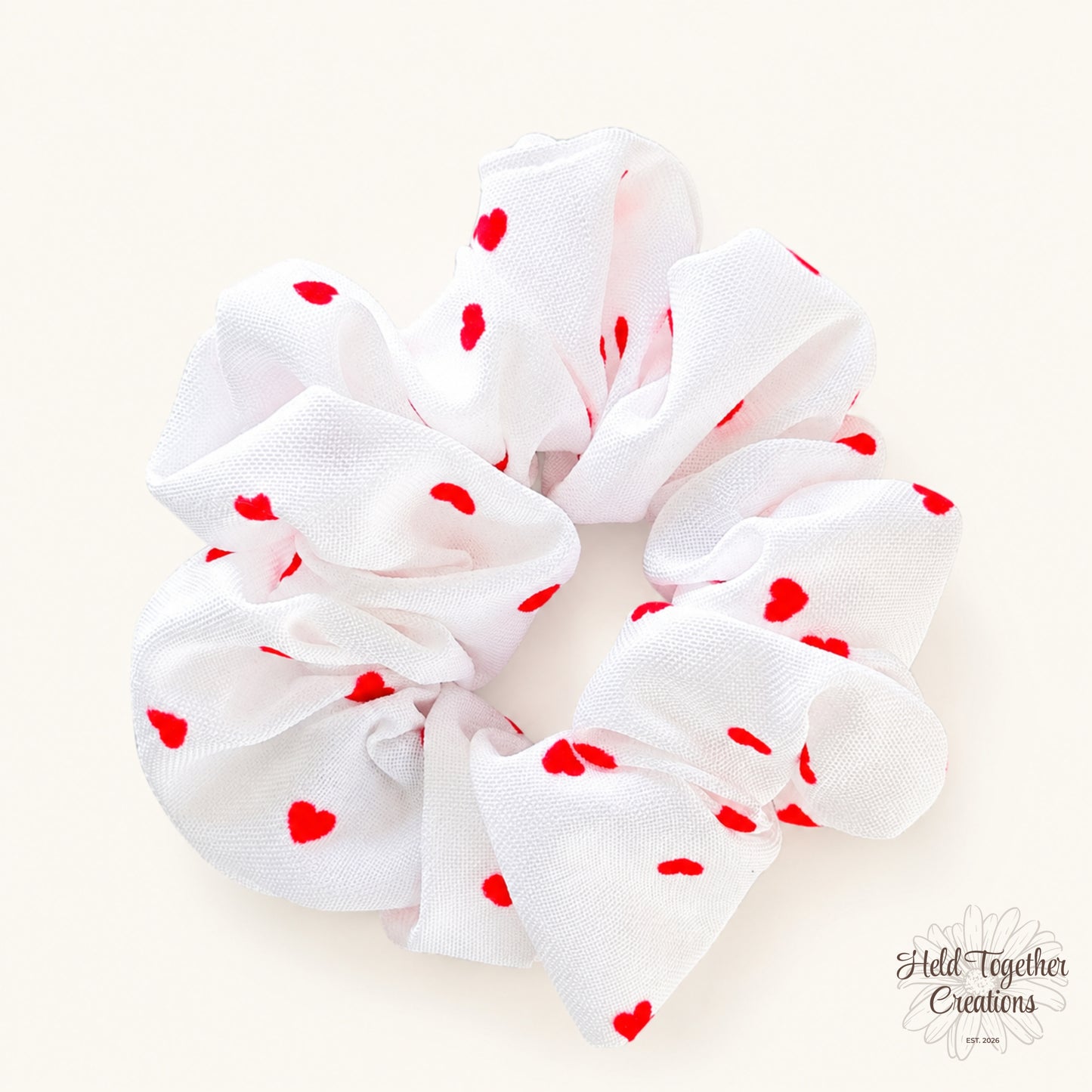 White velvet-style scrunchie with red heart print on a warm ivory background.