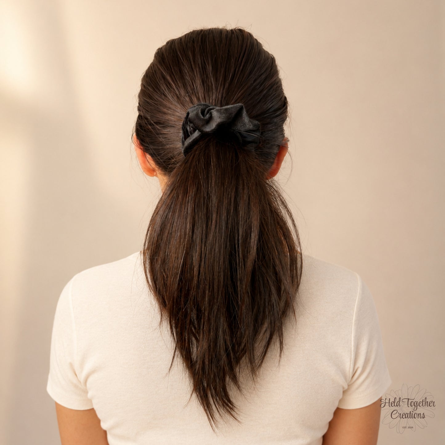 Black velvet handmade scrunchie with white HTC label on a warm neutral background.